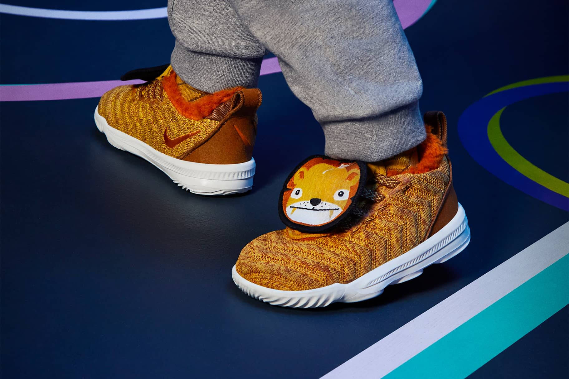 Nike Shoes 桌布 壁紙 — 兒童腳部特寫，穿著橙色獅子主題運動鞋，站在色彩繽紛的球場地板上。