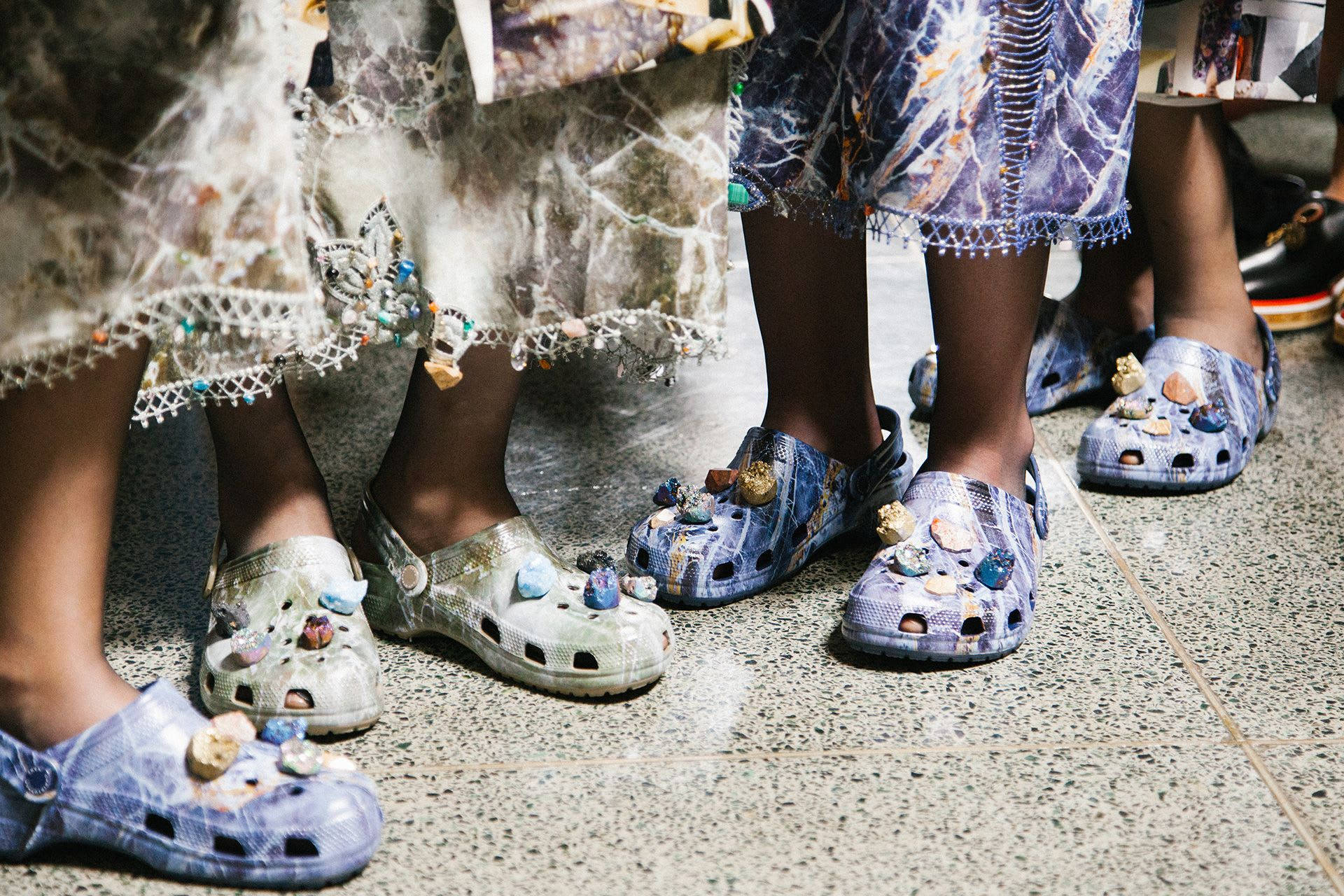 Crocs 桌布 壁紙 — 兒童腳部特寫，穿著色彩繽紛、帶有珠飾的 Crocs 鞋，站在斑點地板瓷磚上。