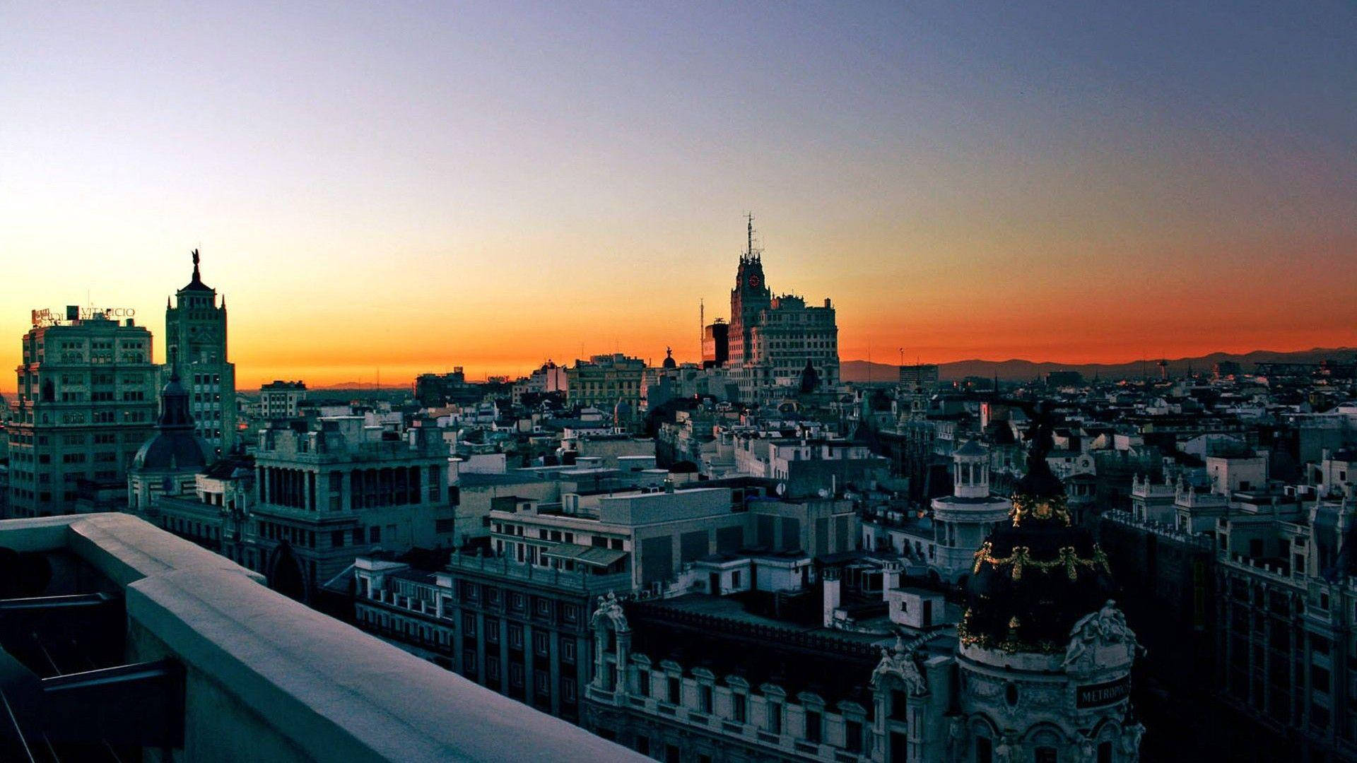 Madrid 桌布 壁紙 — 全景日落景觀，俯瞰密集的歐洲城市天際線，華麗建築在火紅橙色和紫色天空的映襯下形成剪影。