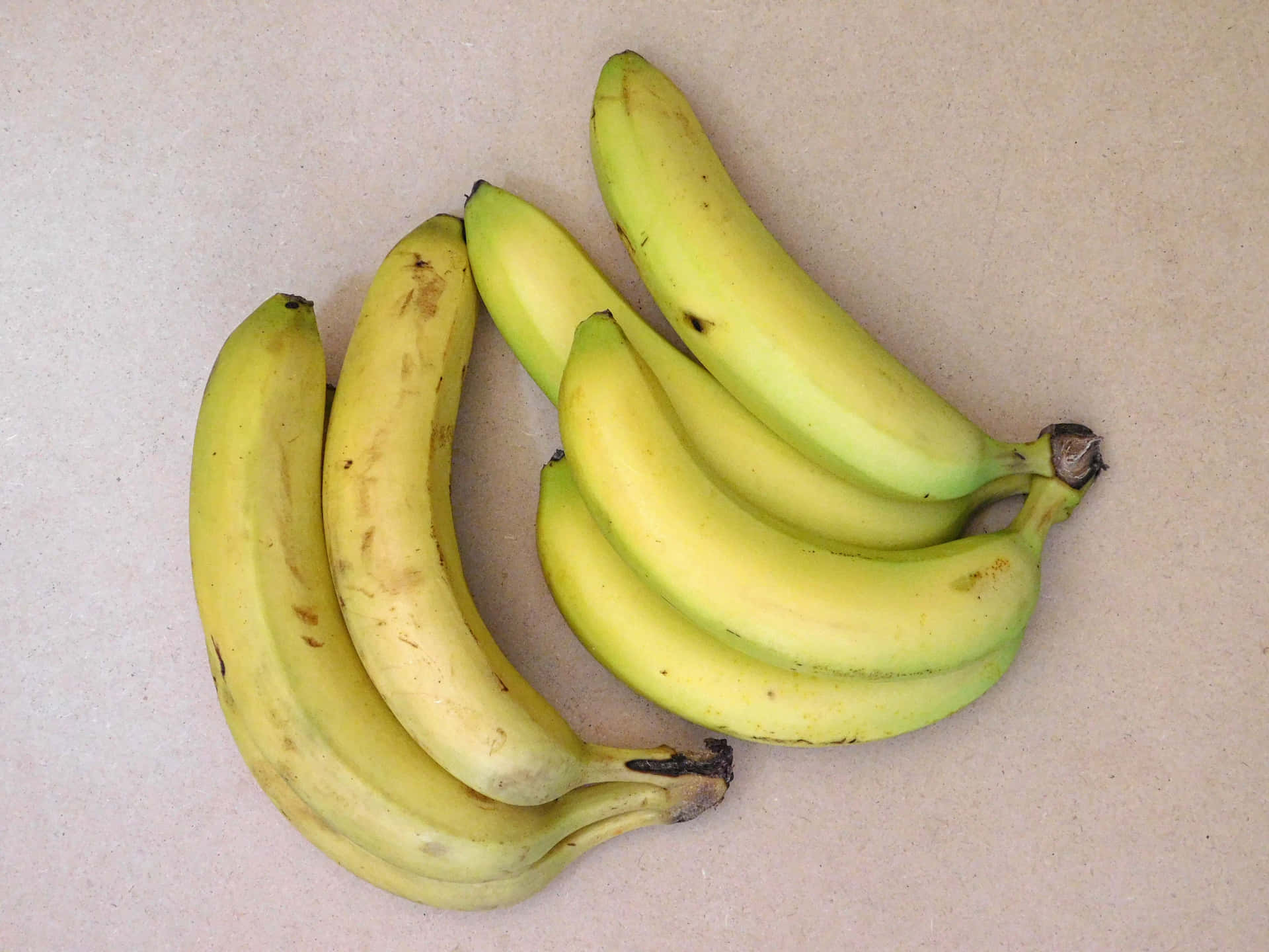 Bananas 壁紙 — 兩串成熟的黃色香蕉帶有棕色斑點，放在淺米色表面上。