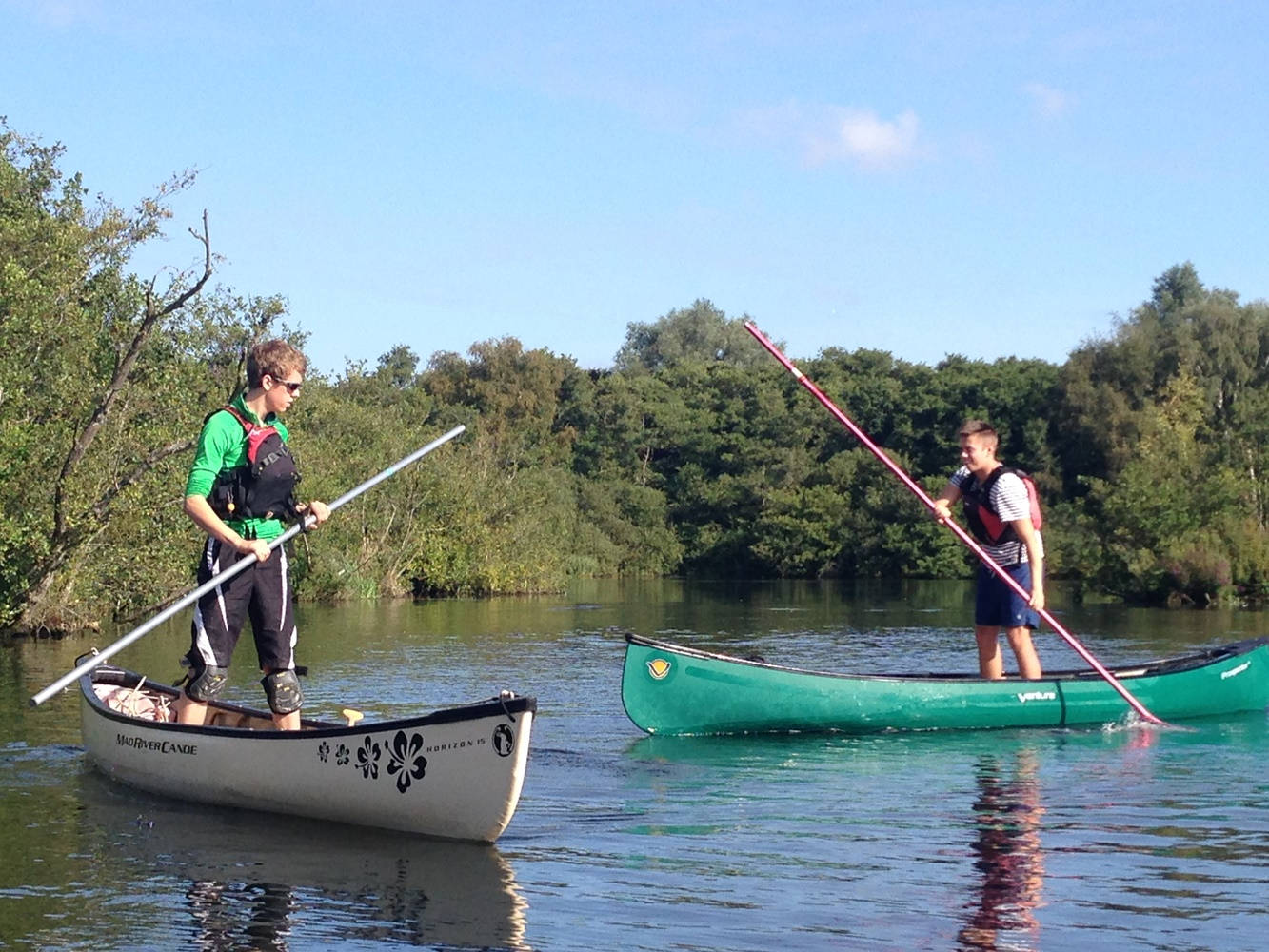 Rowing 桌布 壁紙 — 兩人在平靜的水面上划獨木舟，四周綠樹成蔭，天空湛藍清澈。