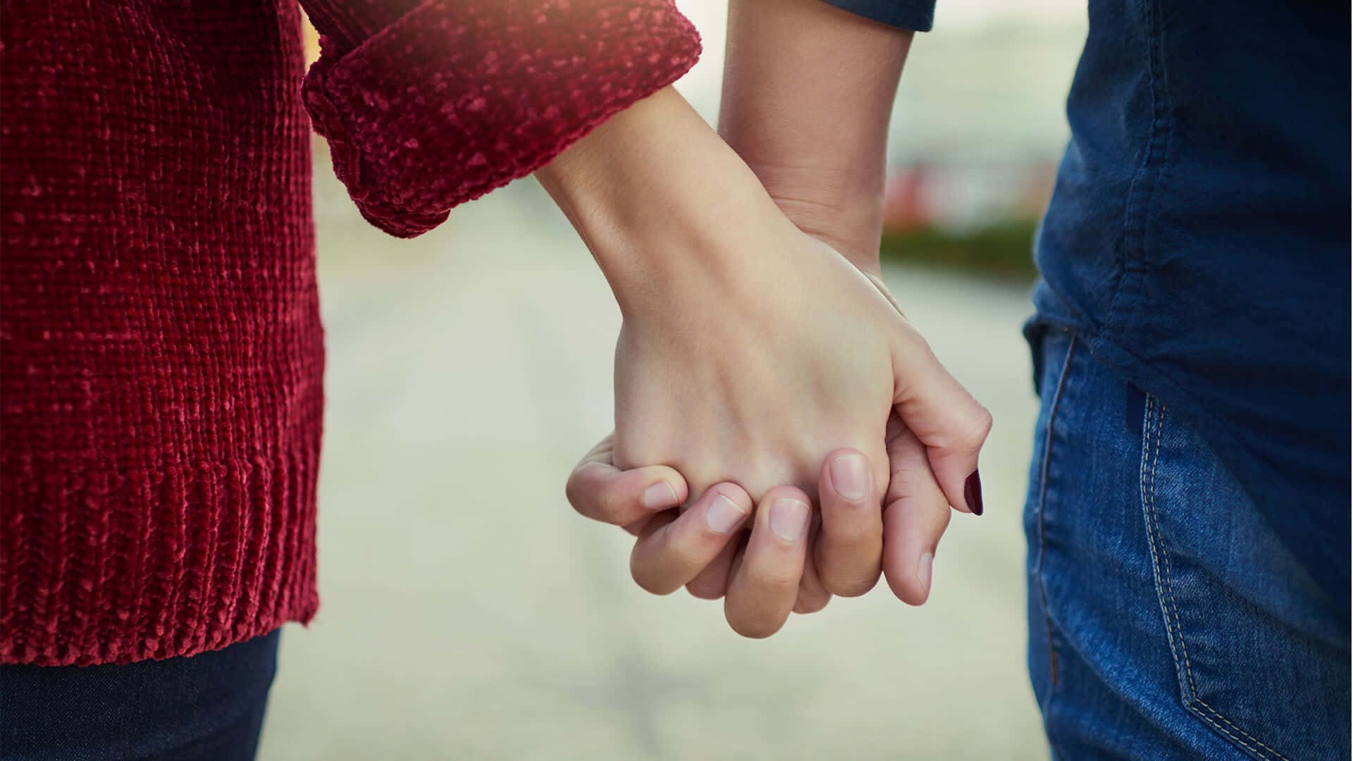 Holding Hands 桌布 壁紙 — 兩人在特寫鏡頭中緊握雙手，柔和陽光突顯他們交織的手指和帶有紋理的衣物。