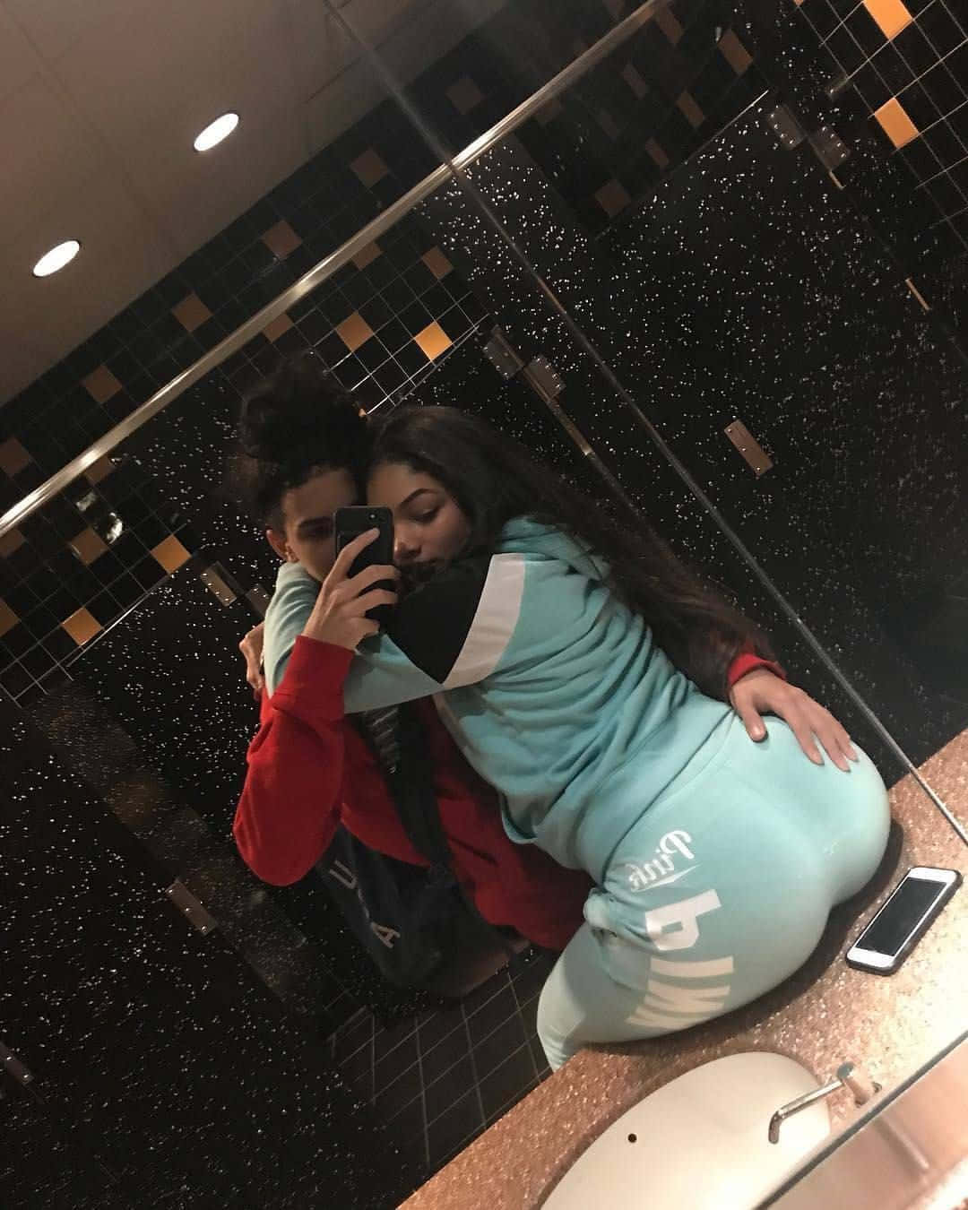 Freaky Couple 桌布 壁紙 — 兩人在現代浴室中擁抱，同時對著鏡子自拍，浴室有黑色斑點瓷磚和溫暖燈光。