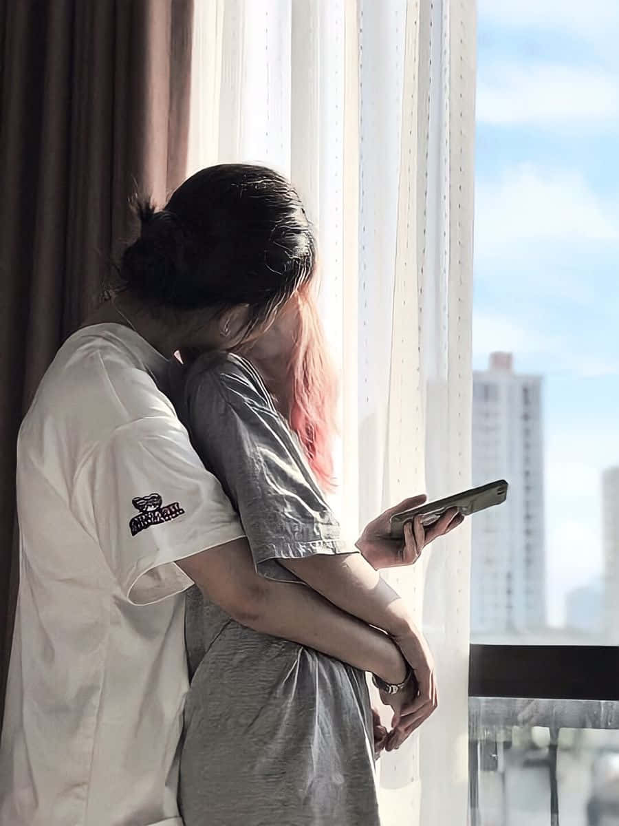 女同志 桌布 壁紙 — 兩人在陽光照射的窗邊擁抱，窗外可見城市建築。