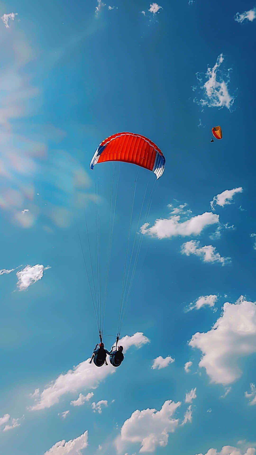 Parachute and blue sky 壁紙 — 兩人在鮮豔的紅藍相間降落傘下，翱翔於點綴著蓬鬆白雲的明亮藍天中。