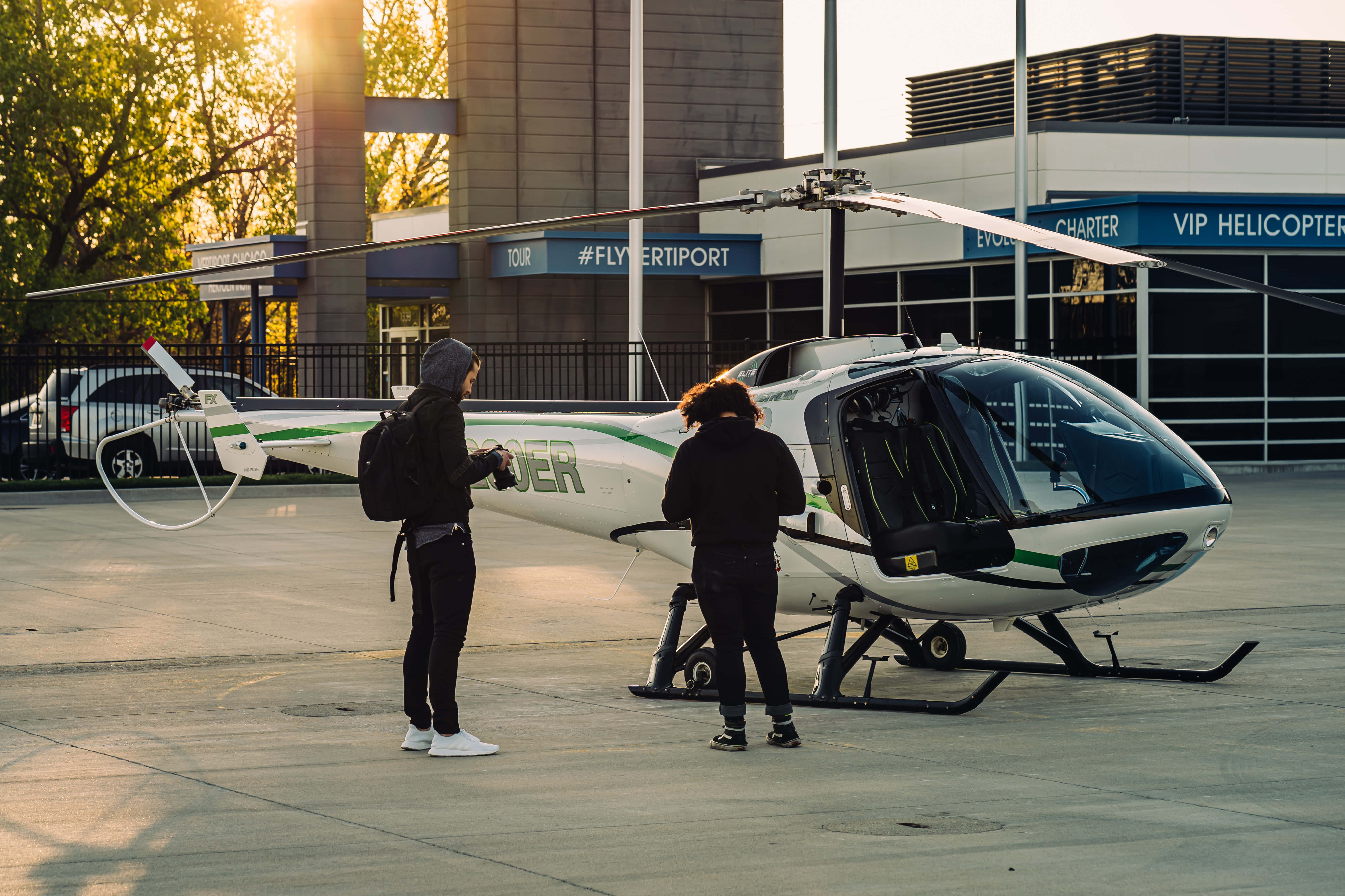 Helicopter 桌布 壁紙 — 兩人站在VIP直升機停機坪的一架白色直升機旁，金色陽光穿過樹林灑落。