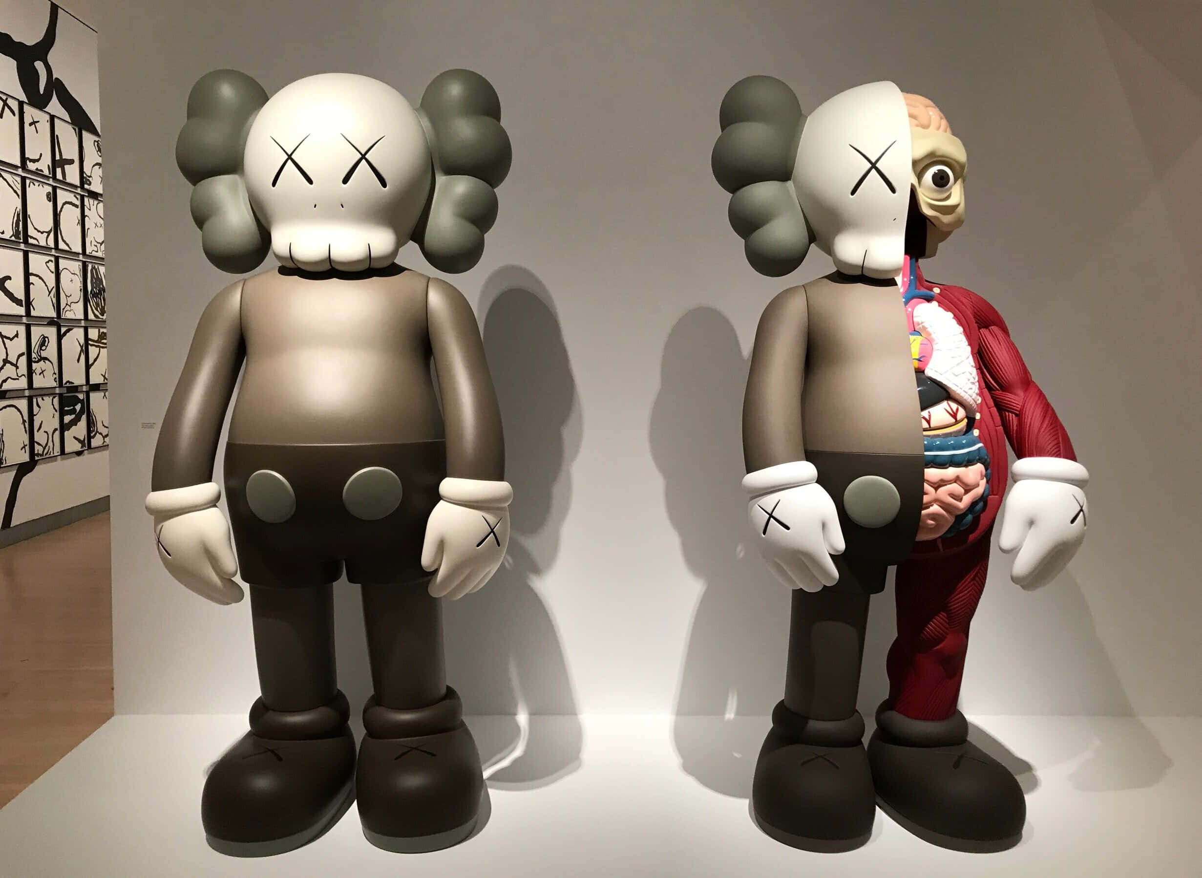 KAWS 桌布 壁紙 — 兩件大型KAWS雕塑並排而立，一件完整無缺，另一件在畫廊環境中顯露內部器官。