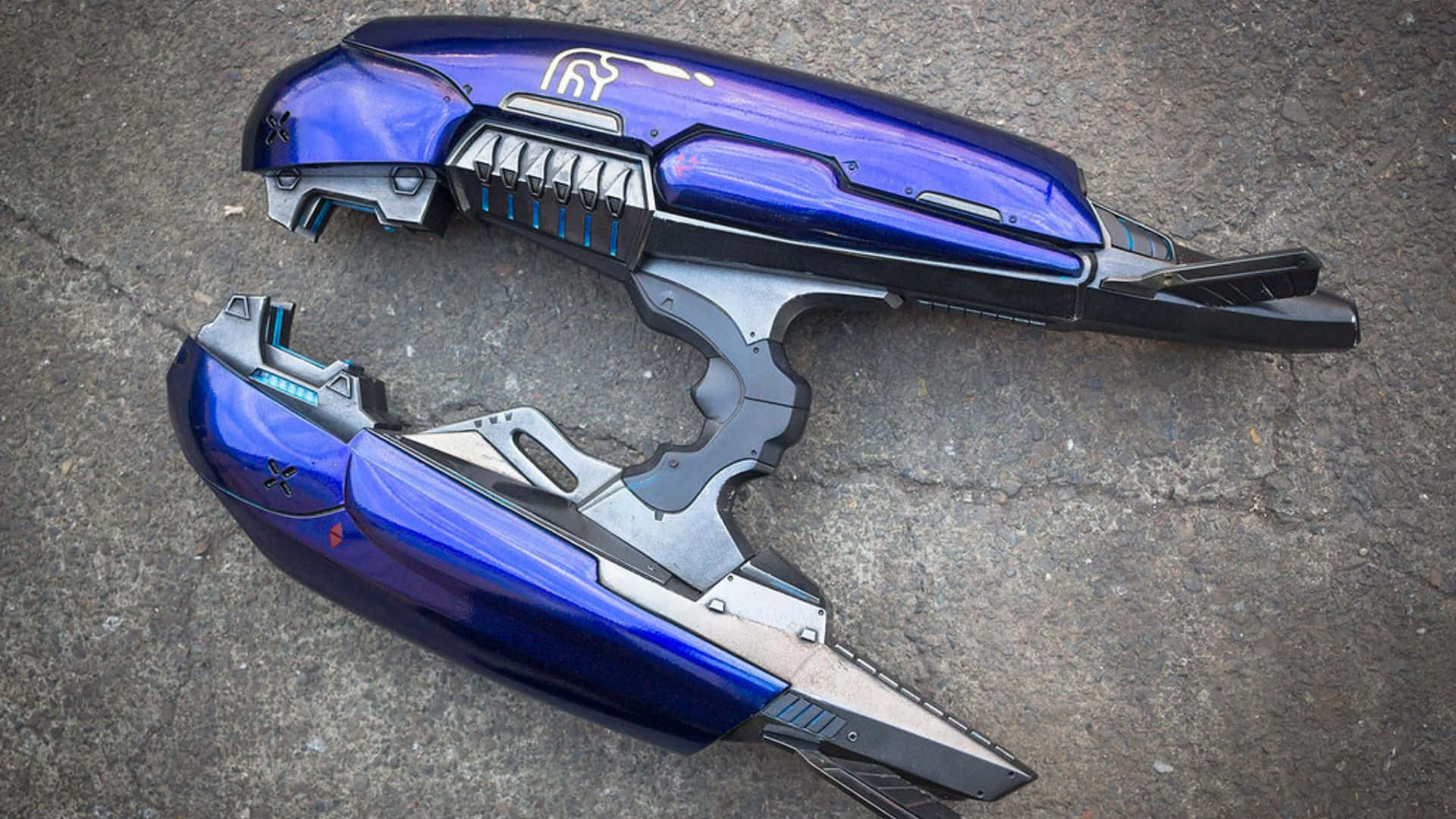Plasma Rifle 桌布 壁紙 — 兩件未來風格的藍銀科幻武器躺在裂開的混凝土路面上。