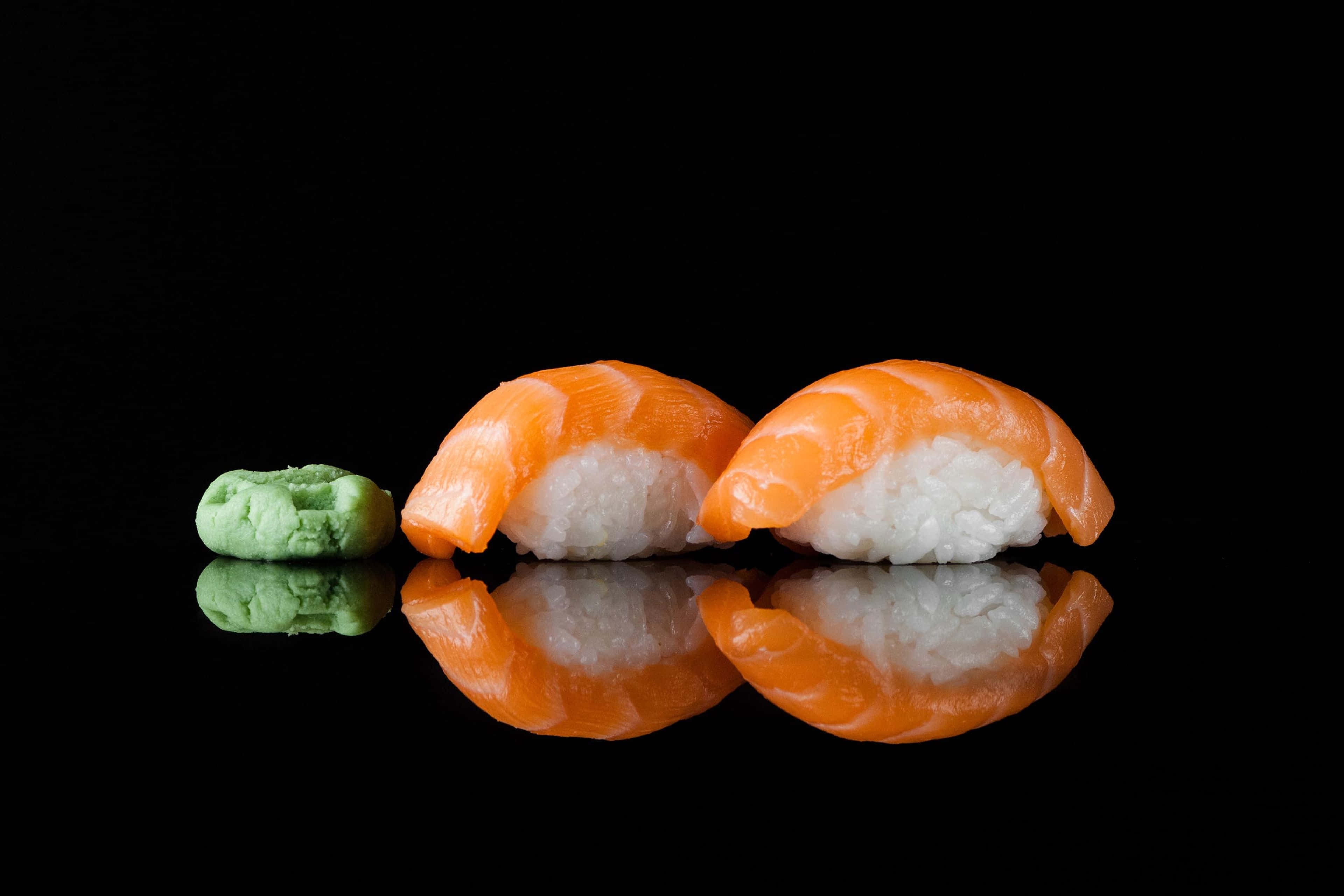 Sushi 桌布 壁紙 — 兩件鮭魚握壽司配芥末，放在光亮的黑色表面上，反射出其鮮豔色彩。