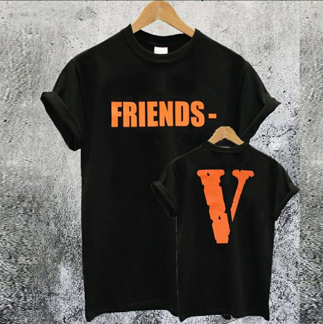 Vlone 桌布 壁紙 — 兩件黑色T恤，上面有橙色「FRIENDS-V」文字，掛在木衣架上，背景是紋理灰色混凝土牆。