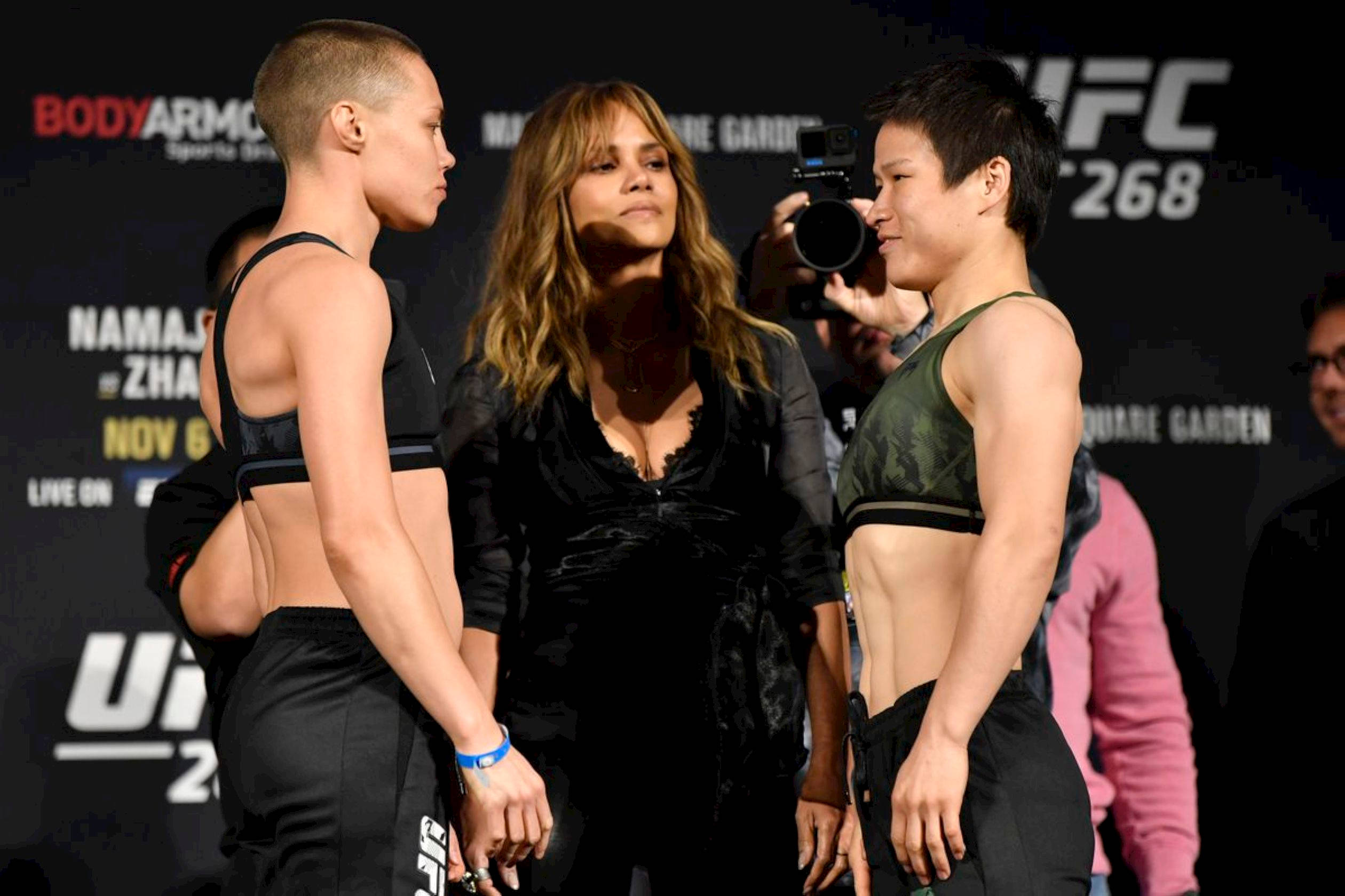 Athletic 桌布 壁紙 — 兩位UFC女拳手在稱重活動中對峙，中間有一位名人。