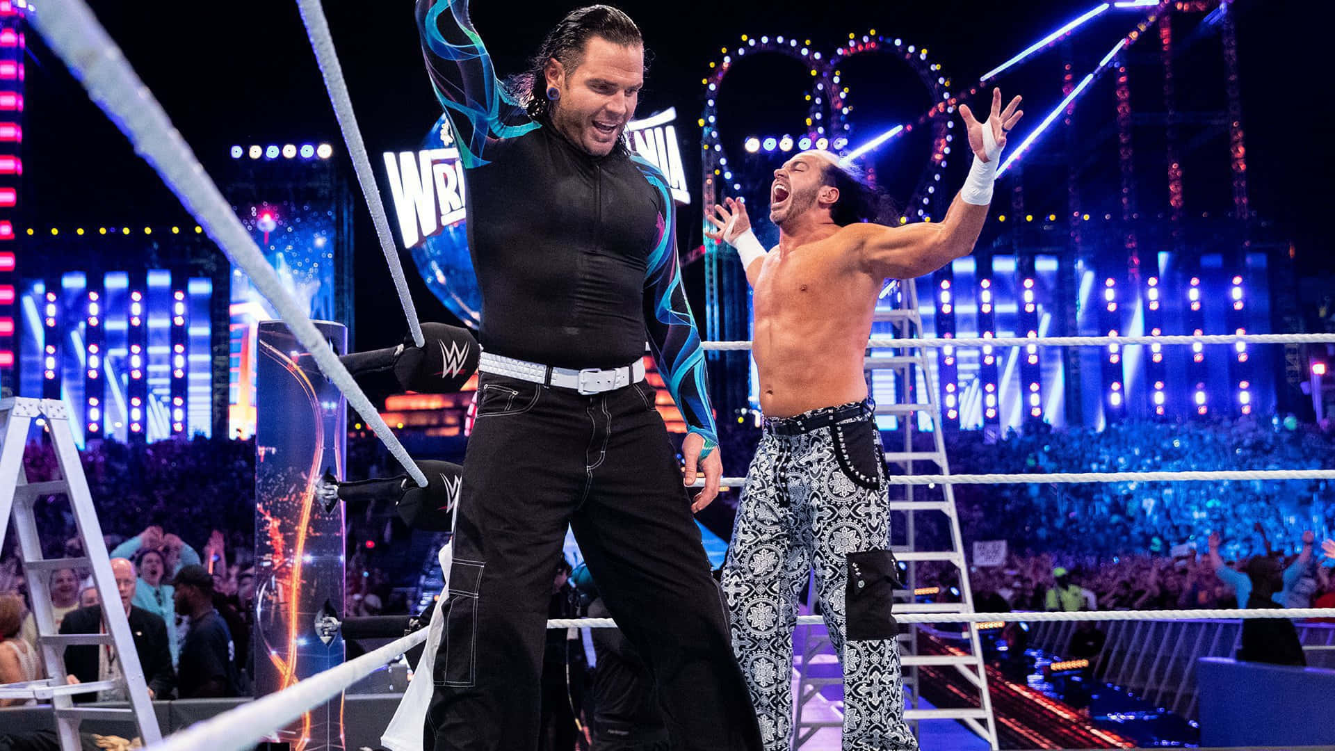 WWE 桌布 壁紙 — 兩位WWE摔角手在燈光明亮的擂台上，身後有梯子和歡呼的人群，勝利慶祝。