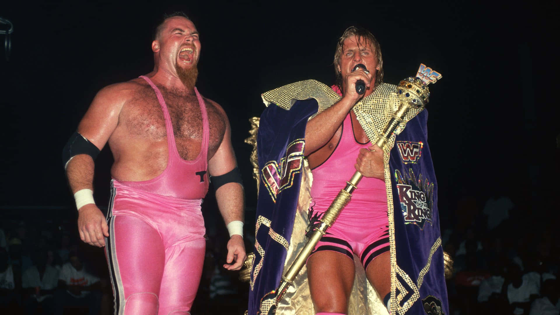 Wrestling 桌布 壁紙 — 兩位WWE摔角手穿著粉紅色緊身褲，一個在尖叫，另一個在舞台上拿著冠軍權杖。