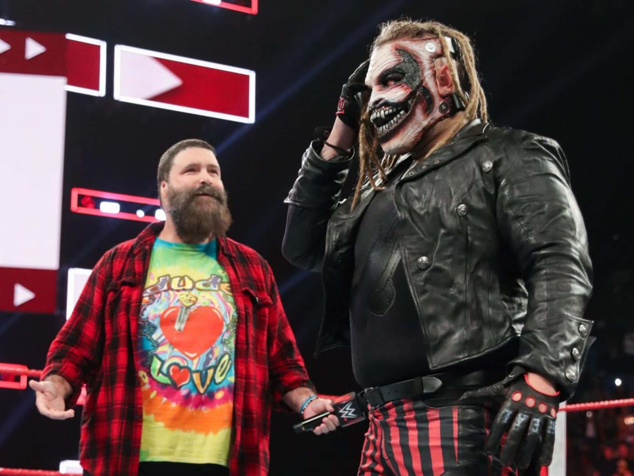 WWE 桌布 壁紙 — 兩位WWE摔角手站在擂台上，一位戴著骷髏面具和皮夾克，另一位穿著紅色格紋襯衫和紮染衫。