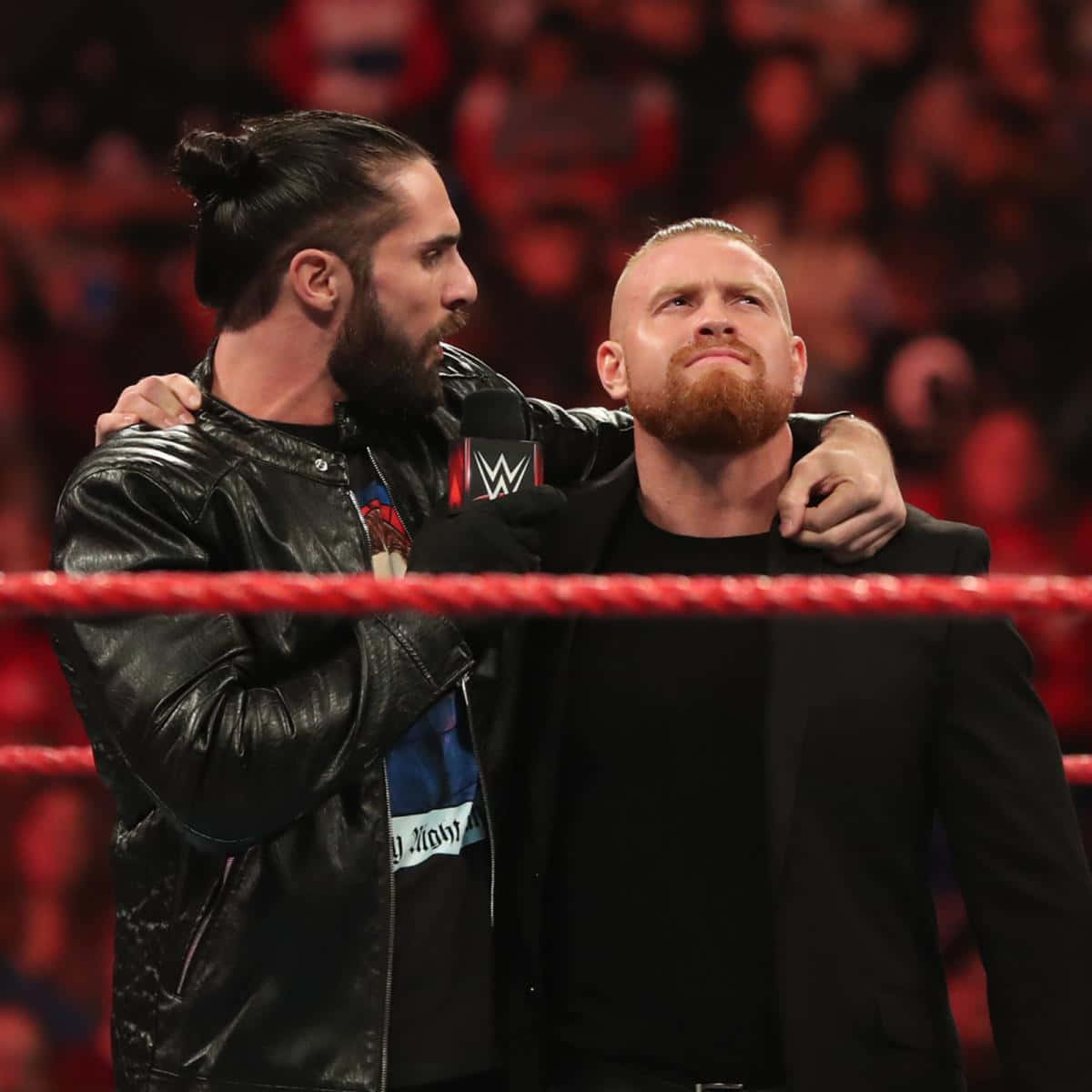 WWE 桌布 壁紙 — 兩位WWE摔角手站在擂台上，其中一人手臂搭在另一人肩上，一支麥克風被舉到他的嘴邊。