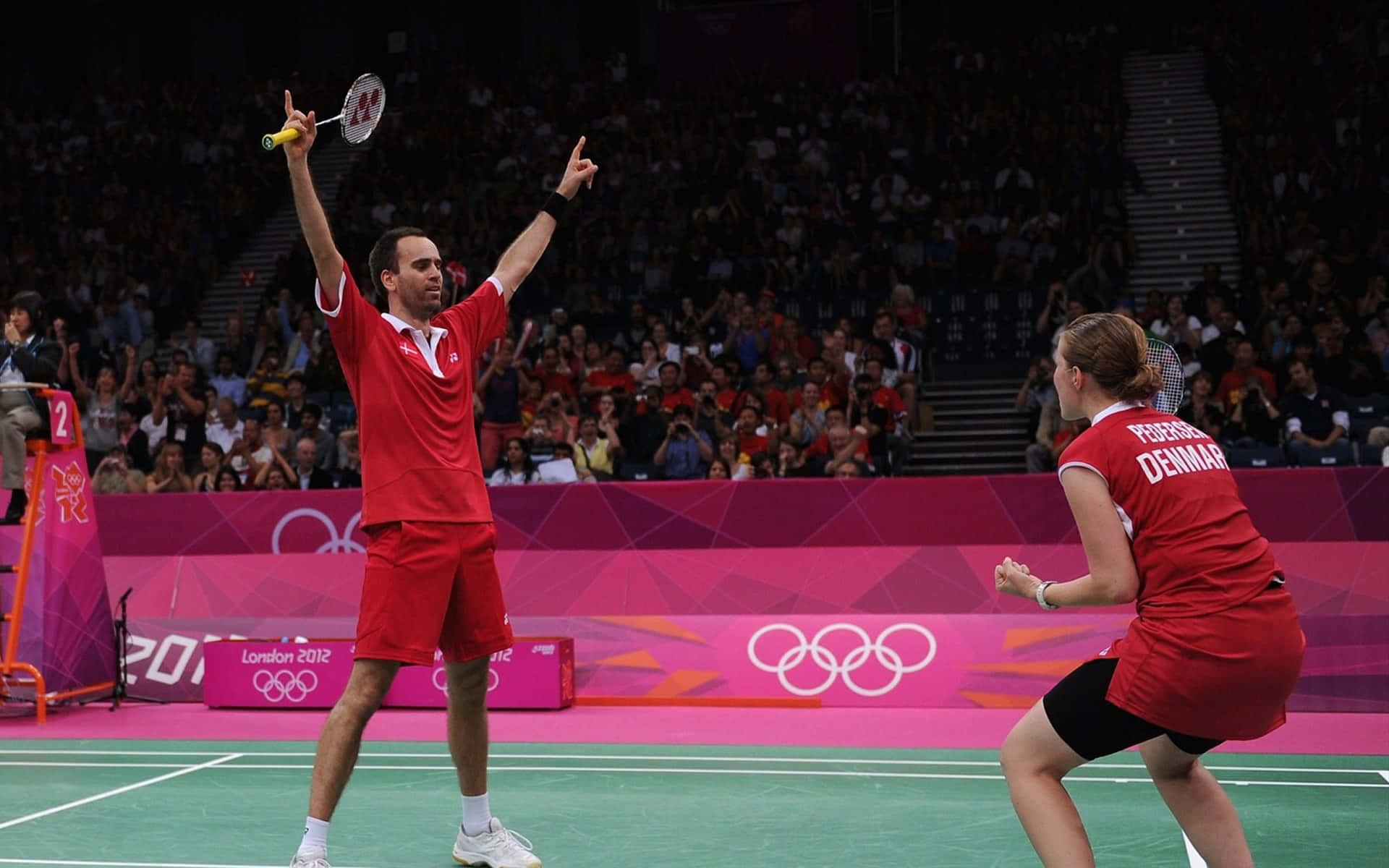 Badminton 桌布 壁紙 — 兩位丹麥羽球選手在燈光明亮的奧運場館中，在歡呼的人群中慶祝得分勝利。