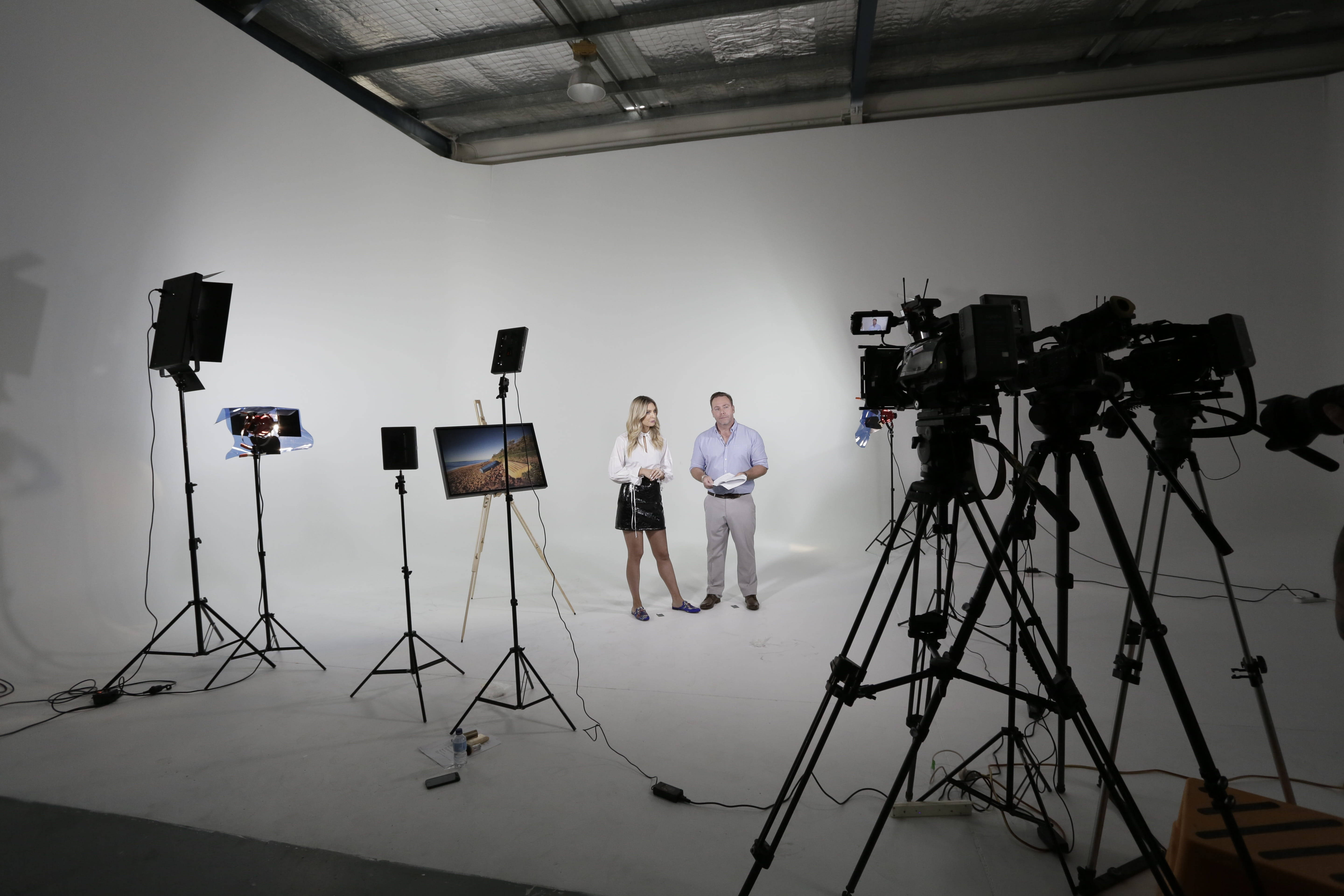 Studio 桌布 壁紙 — 兩位主持人在一個白色錄影室中，周圍有相機、三腳架和顯示風景圖像的顯示器。