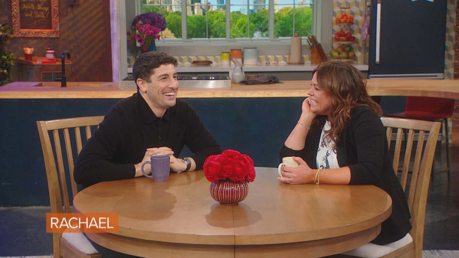 Jason Biggs 桌布 壁紙 — 兩位主持人在工作室廚房佈景中，圍著一張擺有紅玫瑰的圓木桌，邊喝咖啡邊大笑。