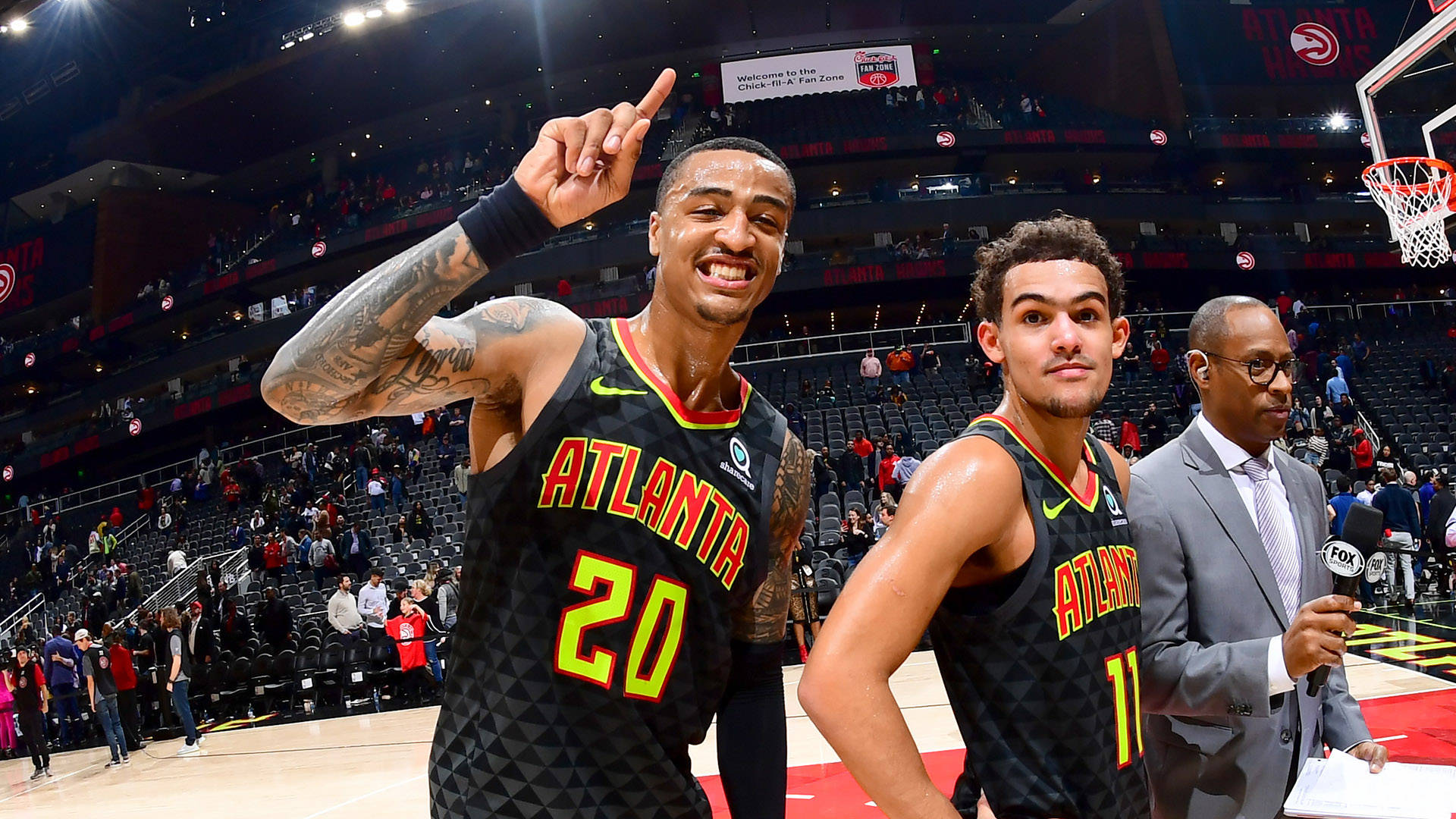 John Collins 桌布 壁紙 — 兩位亞特蘭大老鷹隊籃球球員在球場上慶祝，其中一人向上指，而一名記者站在附近。