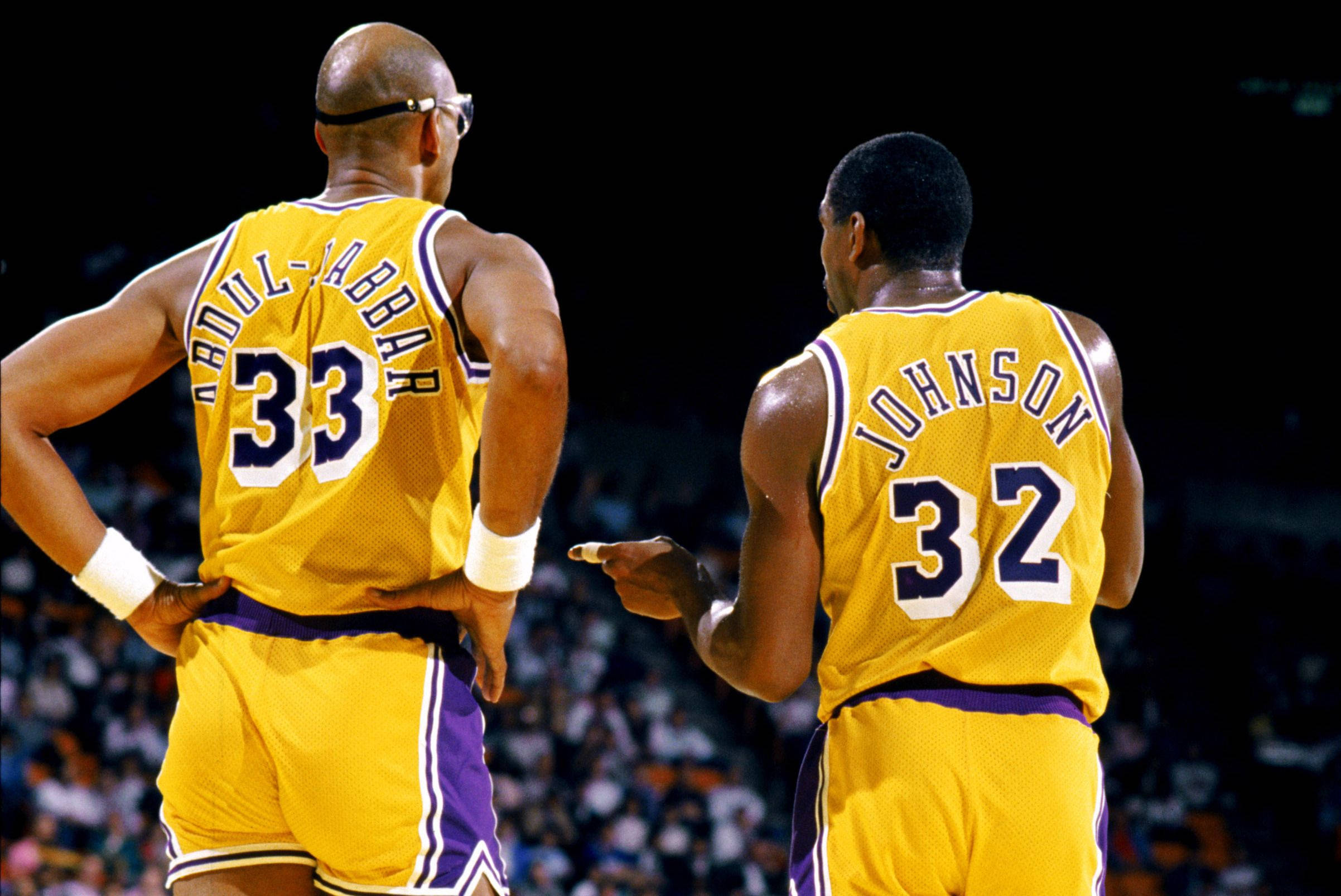 Kareem 桌布 壁紙 — 兩位傳奇湖人籃球運動員身穿黃色球衣，在明亮的場館燈光下於球場上對峙。