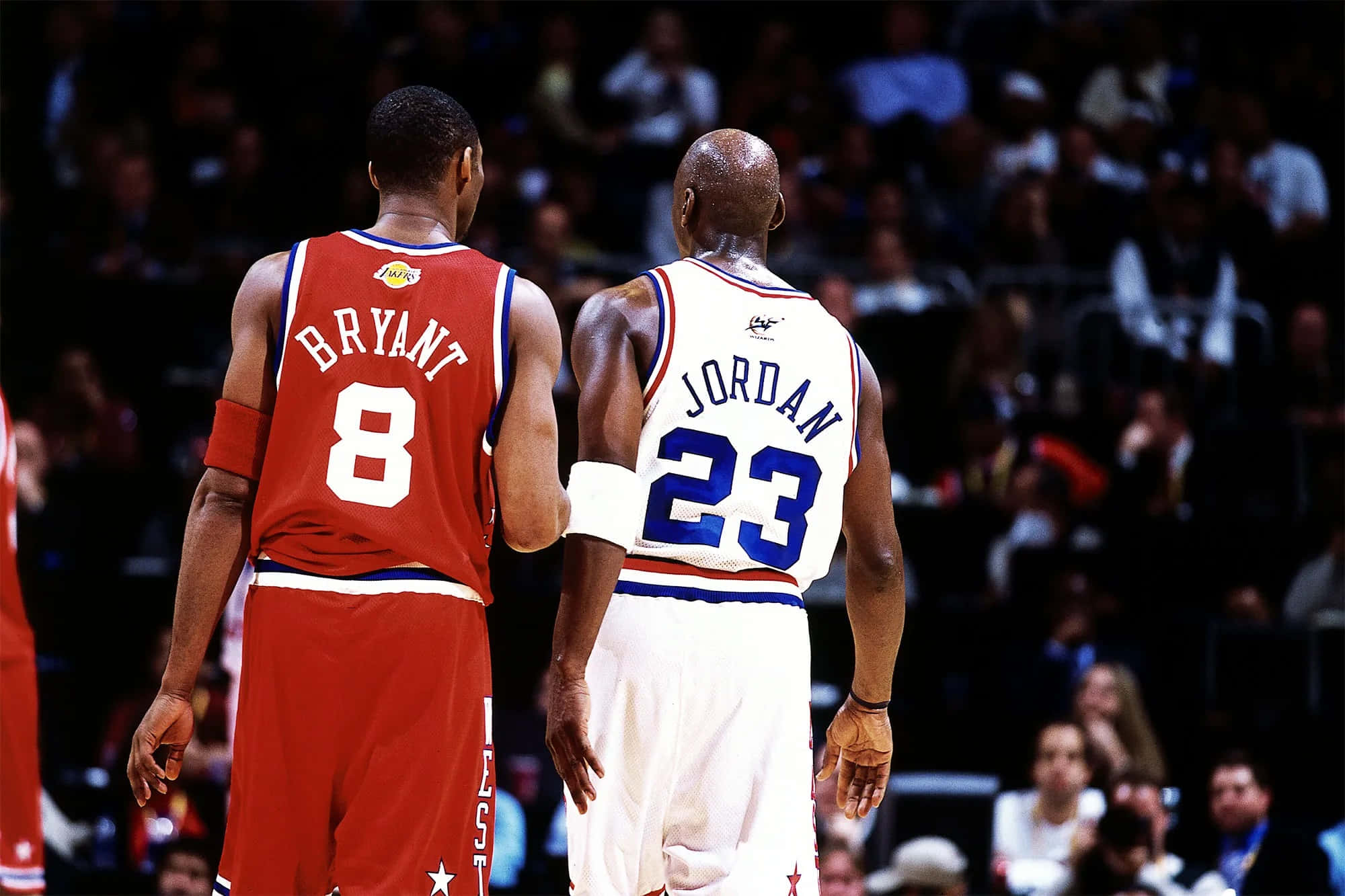 Jordan And Kobe 桌布 壁紙 — 兩位傳奇籃球運動員柯比·布萊恩和麥可·喬丹背對背站在球場上，背景是人群。