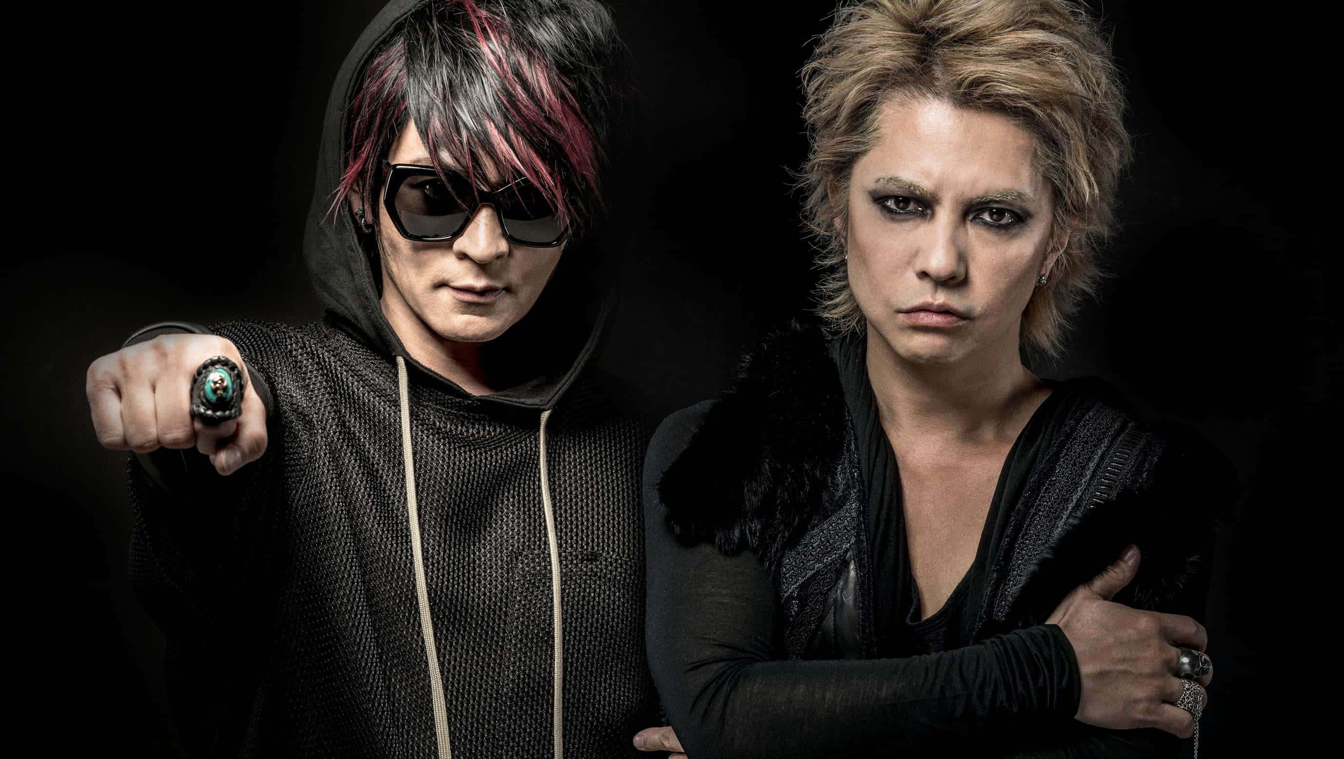 J-rock 桌布 壁紙 — 兩位前衛音樂人，化著大膽妝容，身穿深色服裝，在黑色背景下強烈地擺出姿勢。