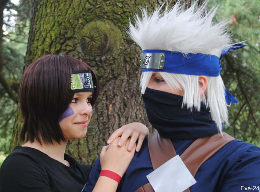Kakashi And Rin 桌布 壁紙 — 兩位動漫角色扮演者穿著火影忍者服裝，在森林環境中一棵長滿苔蘚的樹下擁抱。