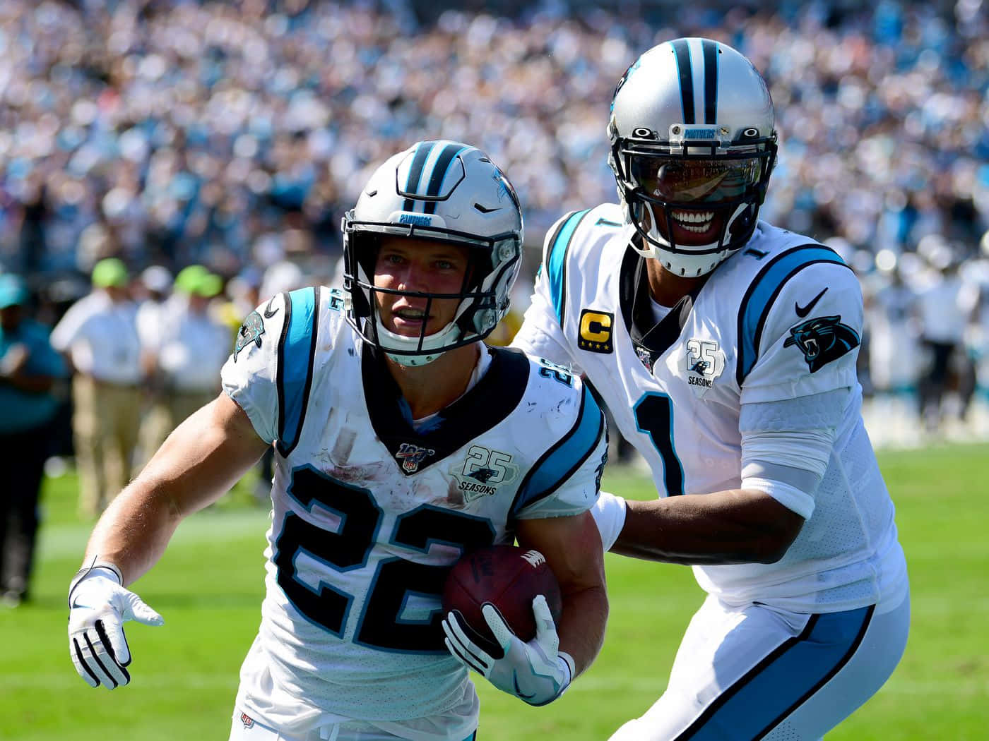 Christian Mccaffrey 桌布 壁紙 — 兩位卡羅萊納黑豹隊美式足球員在陽光明媚的球場上慶祝達陣，背景是歡呼的人群。