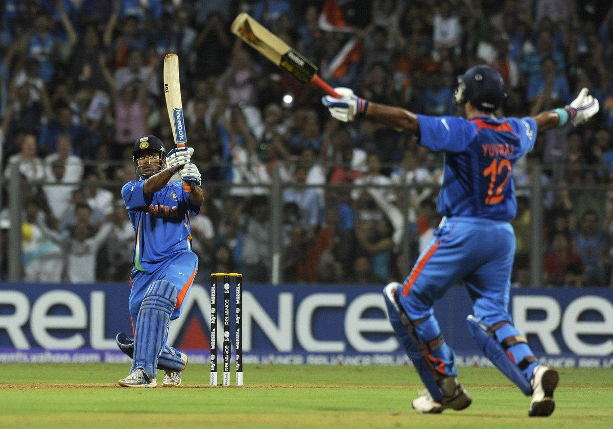 MS Dhoni 桌布 壁紙 — 兩位印度板球手在球場燈光下高舉球棒慶祝六分，背景有球迷歡呼。