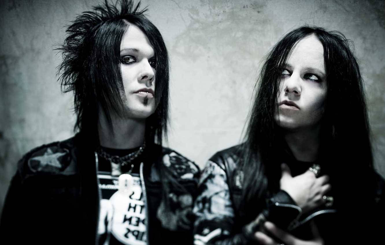 Joey Jordison 桌布 壁紙 — 兩位哥德音樂家，擁有刺蝟般的黑髮和深色妝容，在紋理灰色牆壁前強烈擺姿勢。