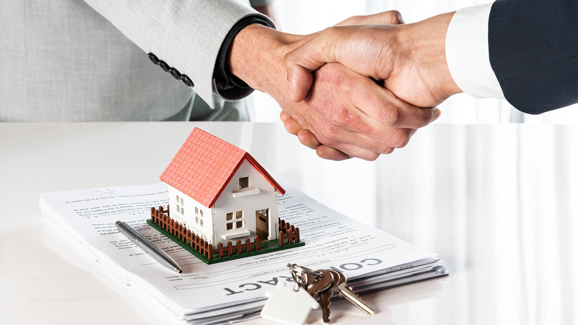 Estate 桌布 壁紙 — 兩位商人在桌上就微型房屋模型合約及鑰匙握手。