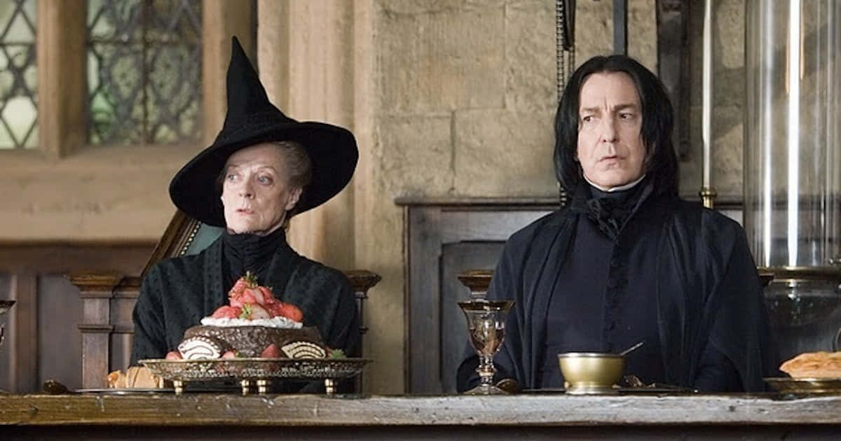 The Hogwarts Professors 桌布 壁紙 — 兩位嚴肅的女巫身穿深色長袍，坐在一張石桌旁，桌上放著草莓蛋糕和高腳杯，身處哥德式石室中。