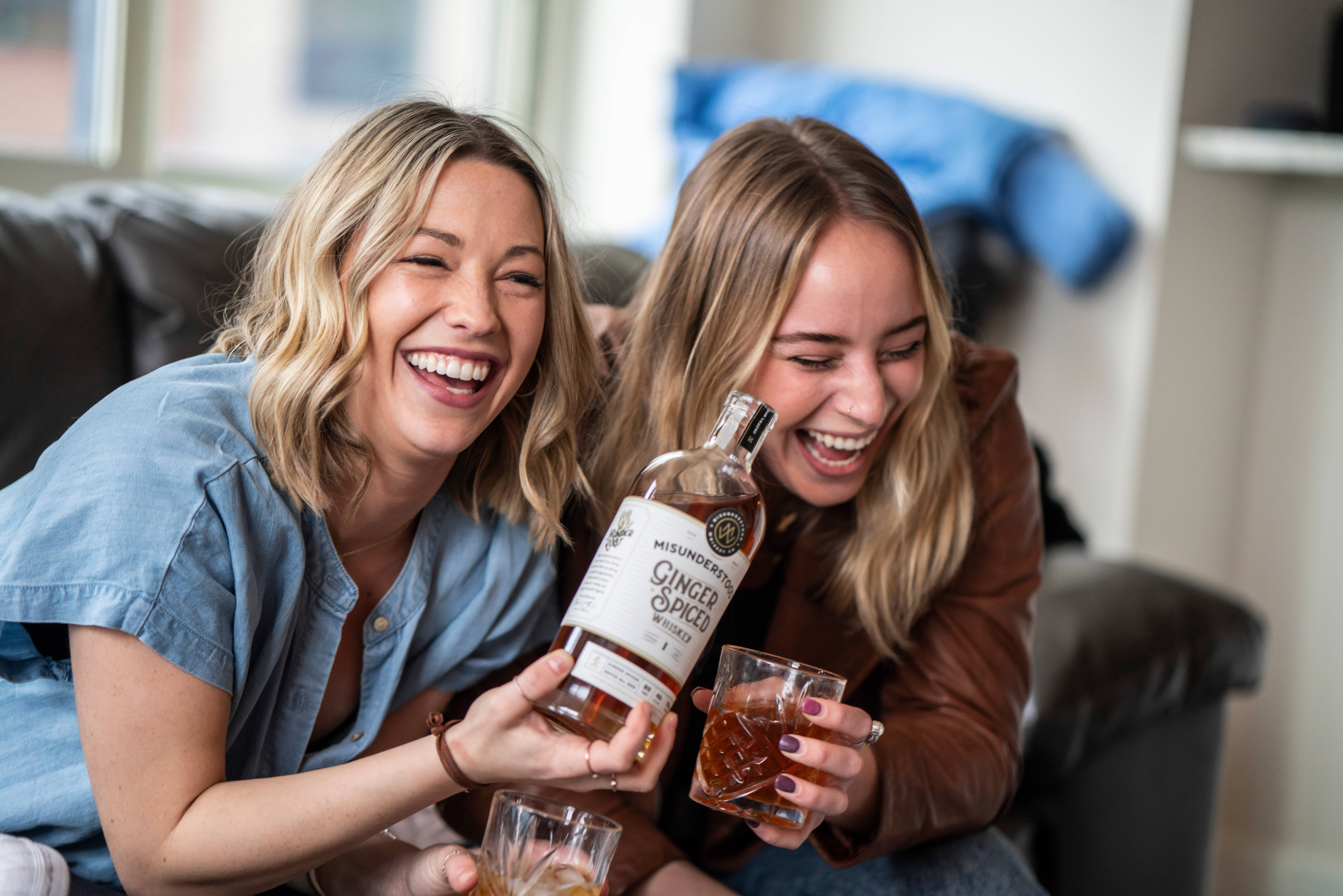 Bachelorette 桌布 壁紙 — 兩位大笑的女性在舒適的客廳沙發上分享一瓶薑味香料威士忌和酒杯。