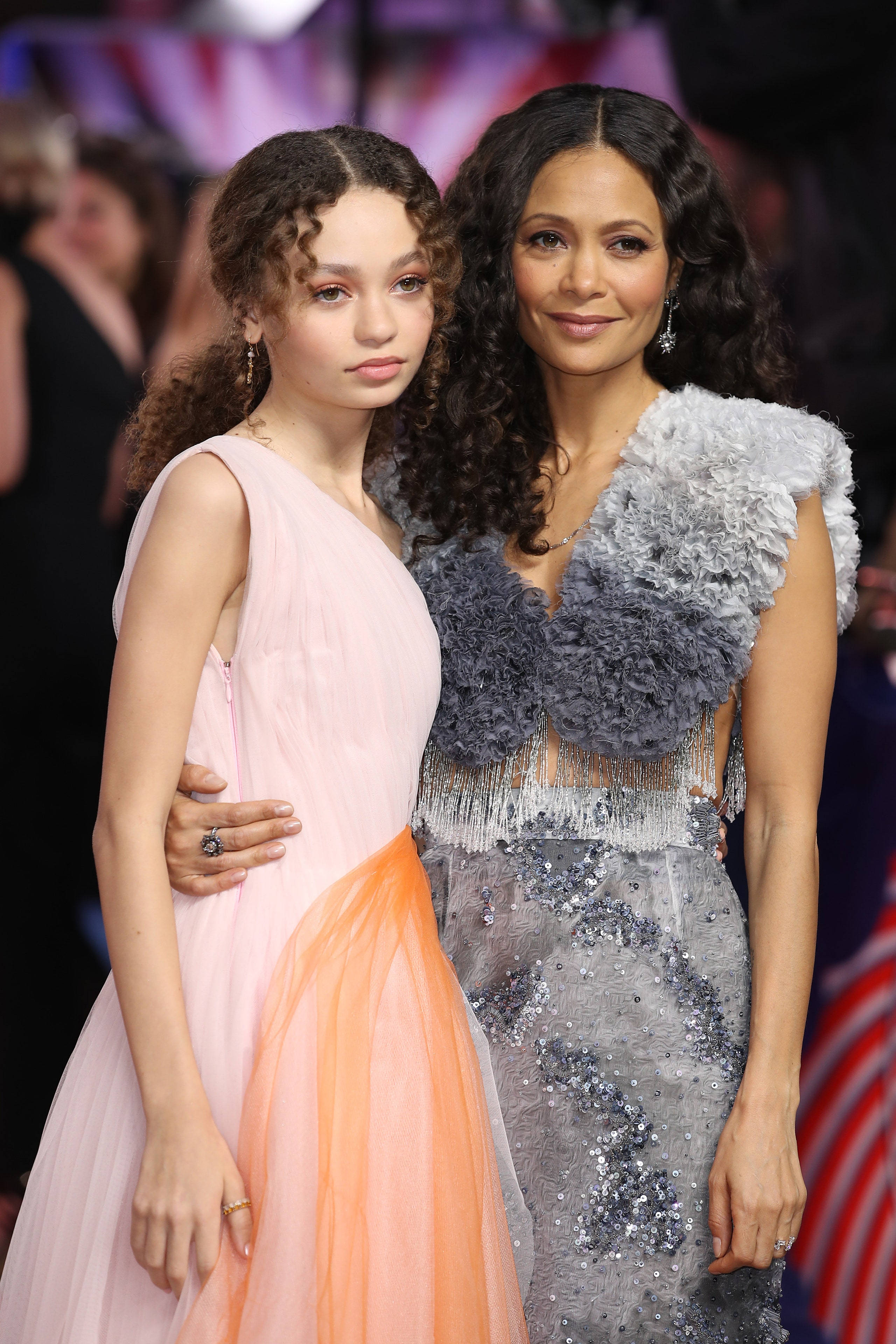 Actress HD 桌布 壁紙 — 兩位女士在紅地毯上優雅地擺姿勢，一位穿著粉紅色和橙色禮服，另一位穿著閃閃發光的銀色亮片連衣裙。