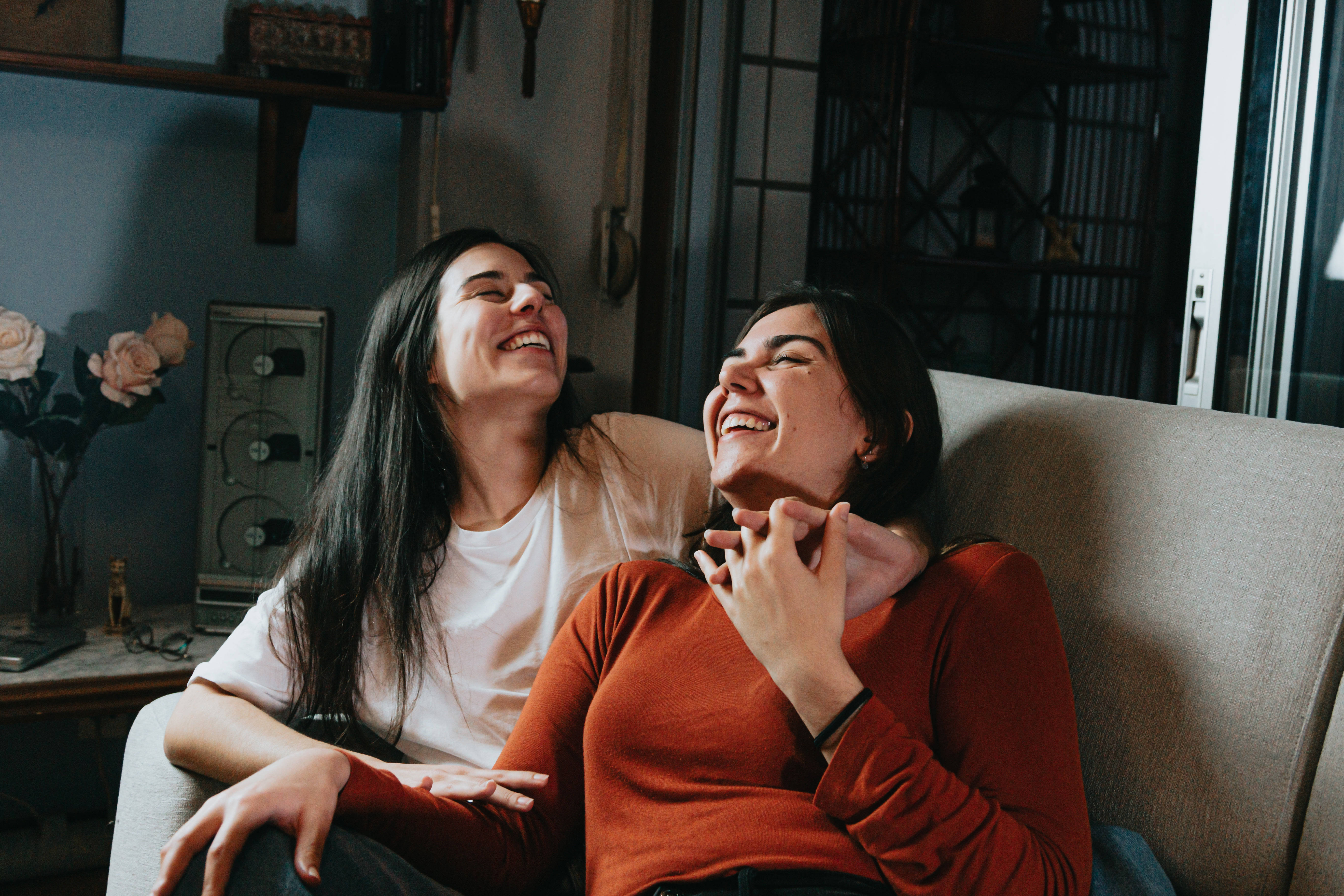 Friendship 桌布 壁紙 — 兩位女士在舒適昏暗的客廳沙發上擁抱並開懷大笑。