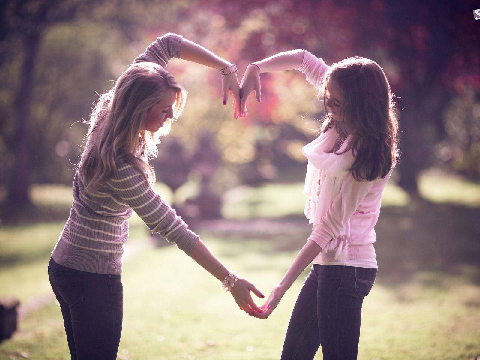 Bff 桌布 壁紙 — 兩位女士在陽光明媚的公園中用手形成心形，背景柔和散景。