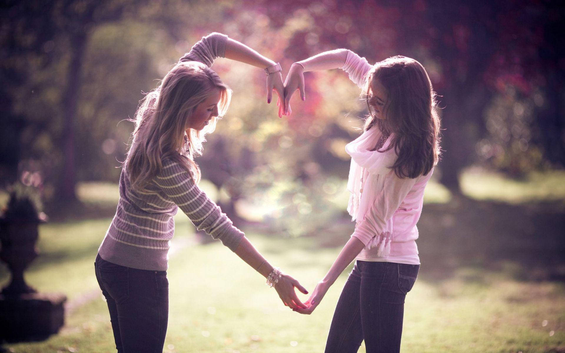 Friendship 桌布 壁紙 — 兩位女士在陽光明媚的公園裡手牽手，用手比出心形。