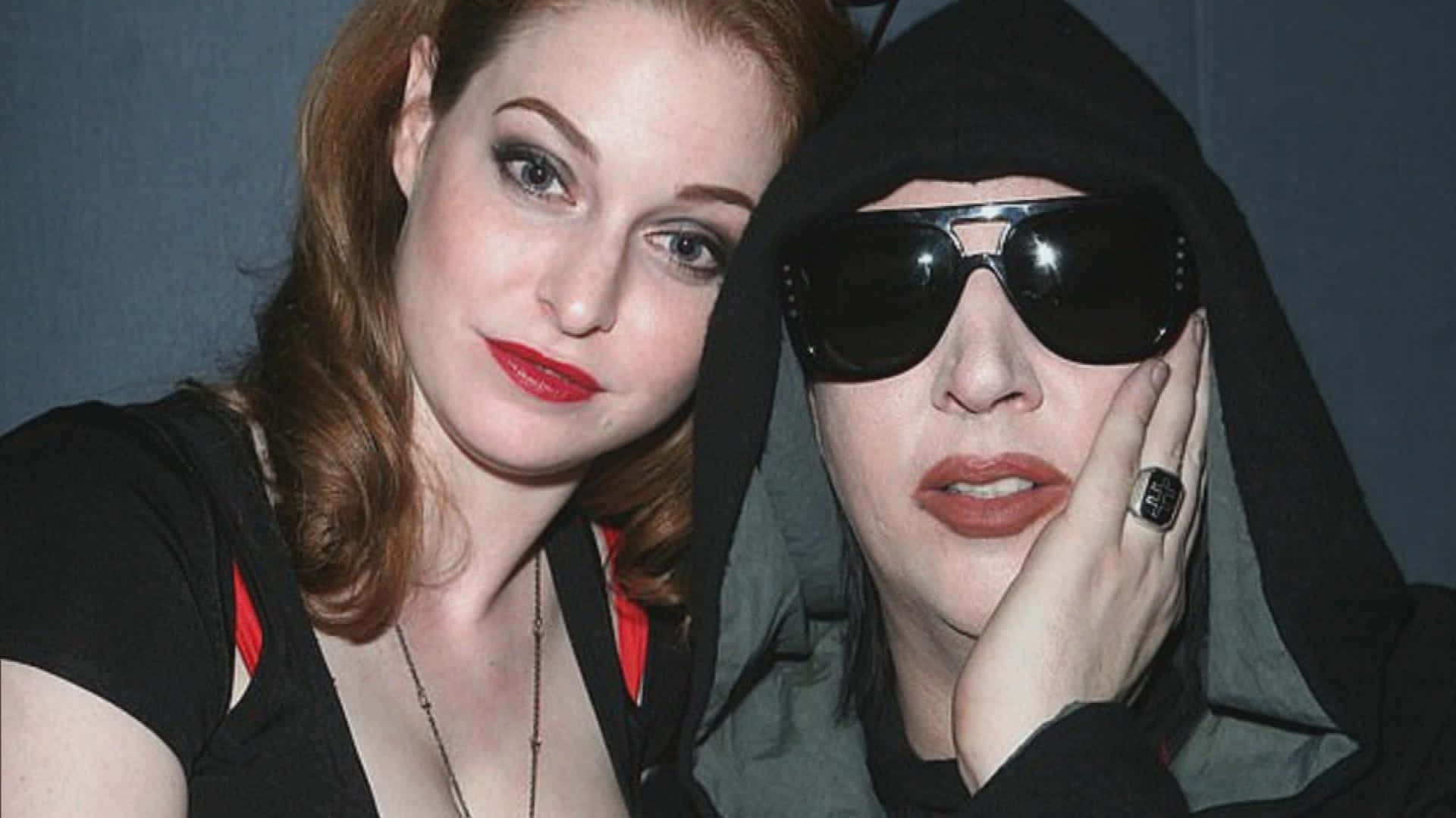 Esmé Bianco 桌布 壁紙 — 兩位女士緊密地擺姿勢，一位有紅髮和鮮豔的紅唇，另一位穿著黑色連帽衫和太陽眼鏡，下巴擱在手上。