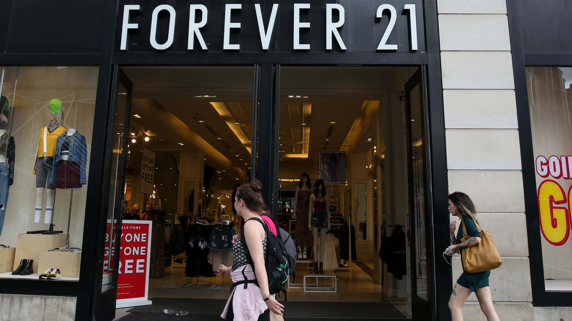 永遠21 桌布 壁紙 — 兩位女士走過一間Forever 21商店，店鋪有明亮的招牌和櫥窗內的模特兒。