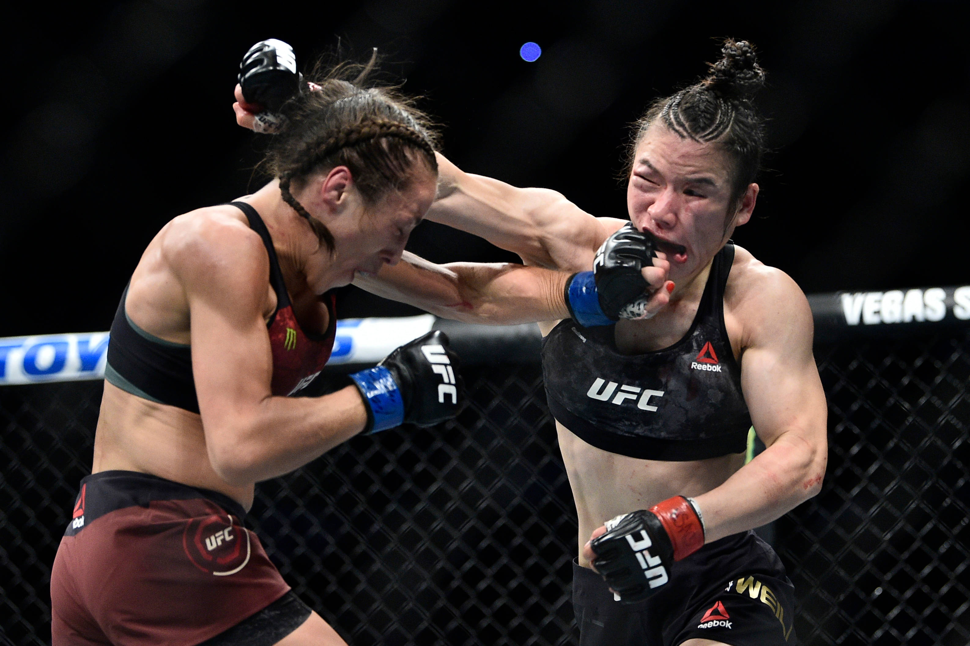 Punch 桌布 壁紙 — 兩位女性MMA拳手在八角籠內進行激烈的UFC比賽，燈光明亮，背景昏暗。