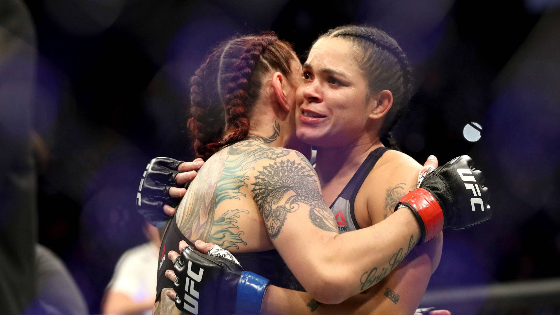 MMA 桌布 壁紙 — 兩位女性MMA拳手在明亮的場館燈光下，於八角籠內賽後情感相擁。
