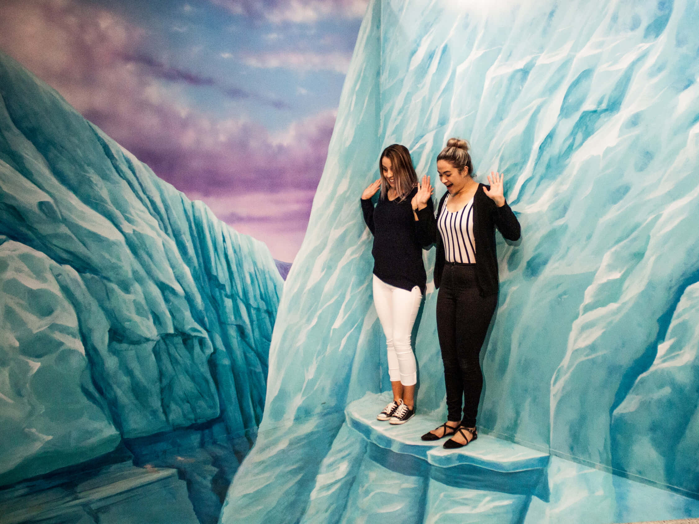 3D 桌布 壁紙 — 兩位女性在3D幻覺展覽中，雙手按在彩繪冰峽谷牆上擺姿勢。