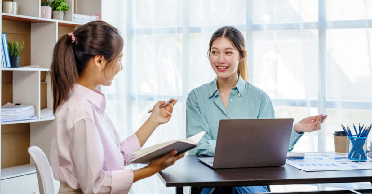 interview 桌布 壁紙 — 兩位女性在光線充足、現代化的辦公室中協作，周圍有整齊的架子。
