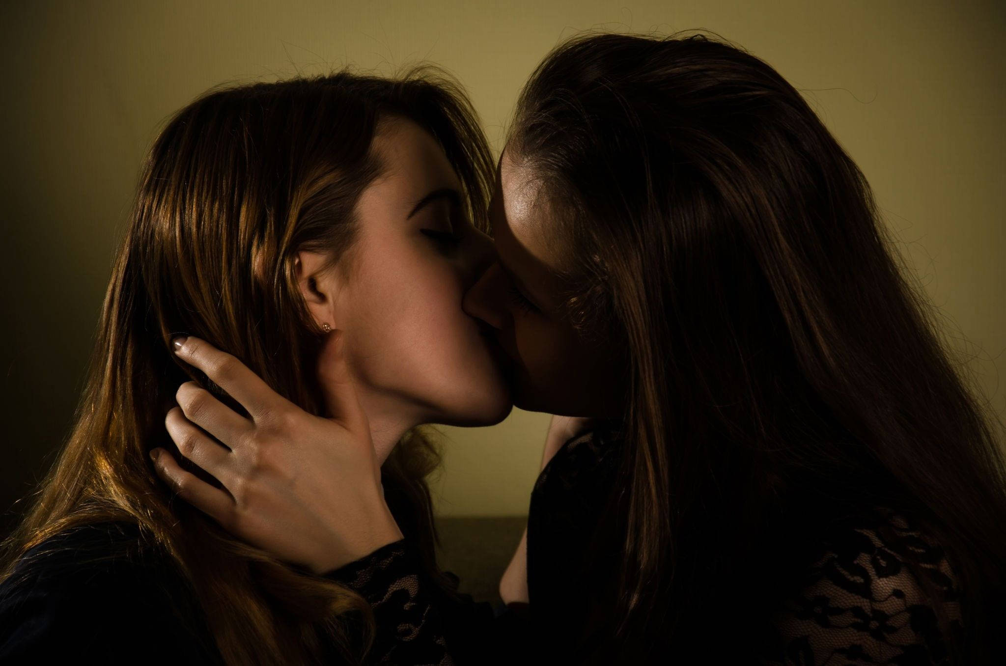 Kissing 桌布 壁紙 — 兩位女性在昏暗溫暖的燈光下親吻，一隻手輕輕托住對方的頸部。