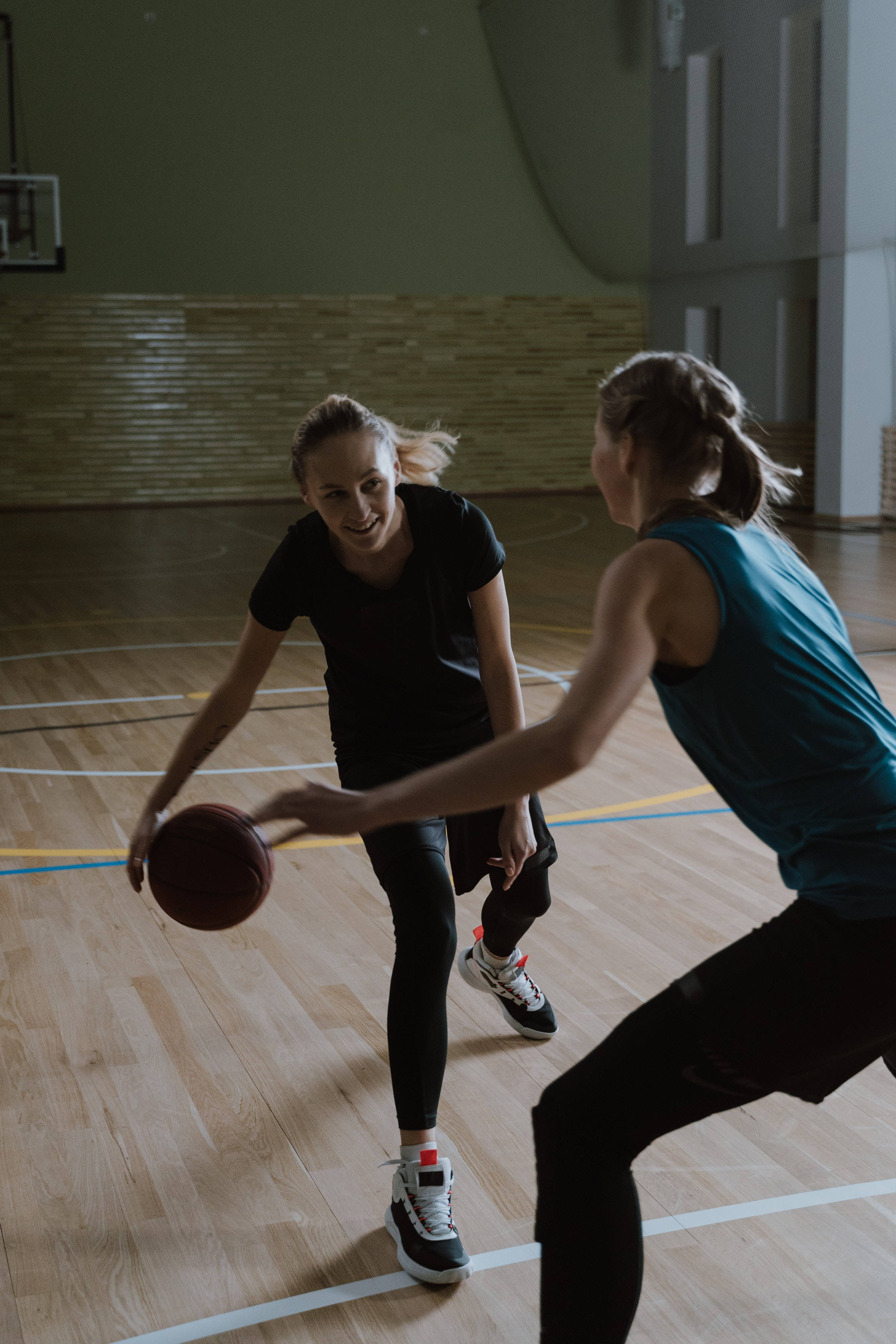 Physical 桌布 壁紙 — 兩位女性在木地板和明亮燈光的體育館中激烈地打籃球。