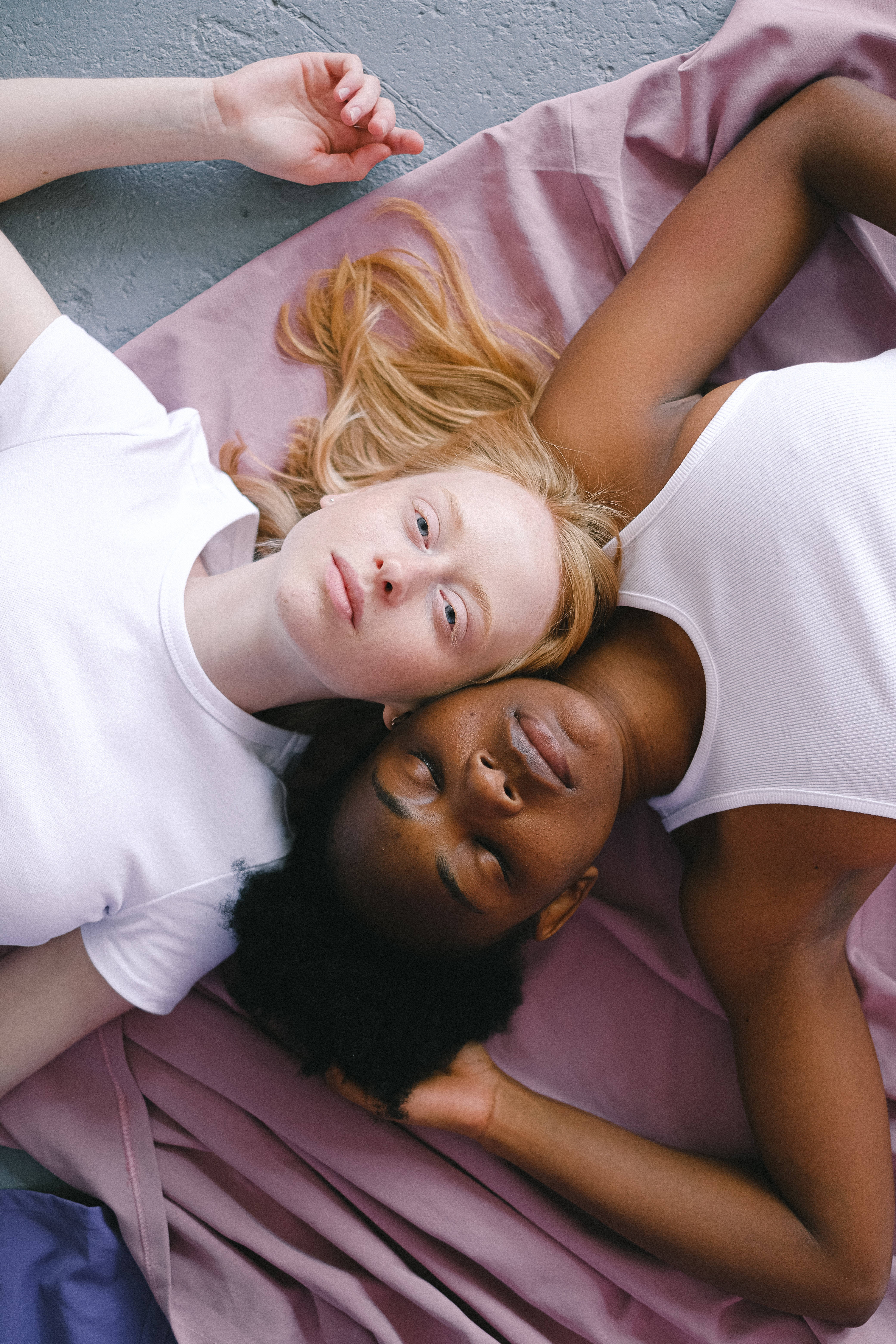 Teenage 桌布 壁紙 — 兩位女性在灰色混凝土地板上的一張柔軟粉紅色毯子上平靜地休息，一位睜著眼睛，另一位閉著眼睛。
