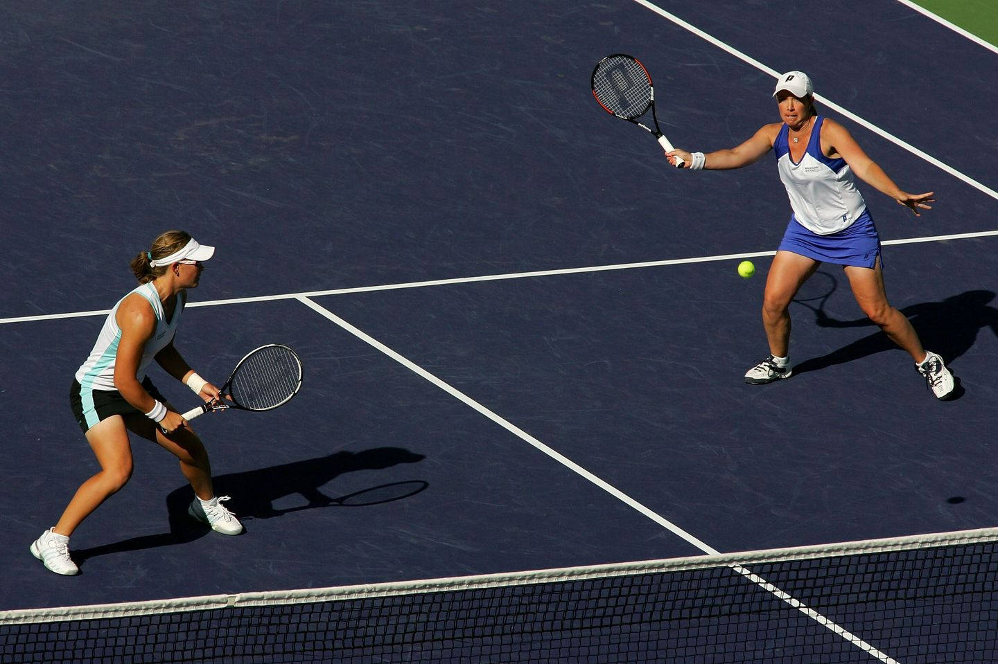 Tennis 桌布 壁紙 — 兩位女網球運動員在明亮的陽光下於藍色硬地球場上比賽。