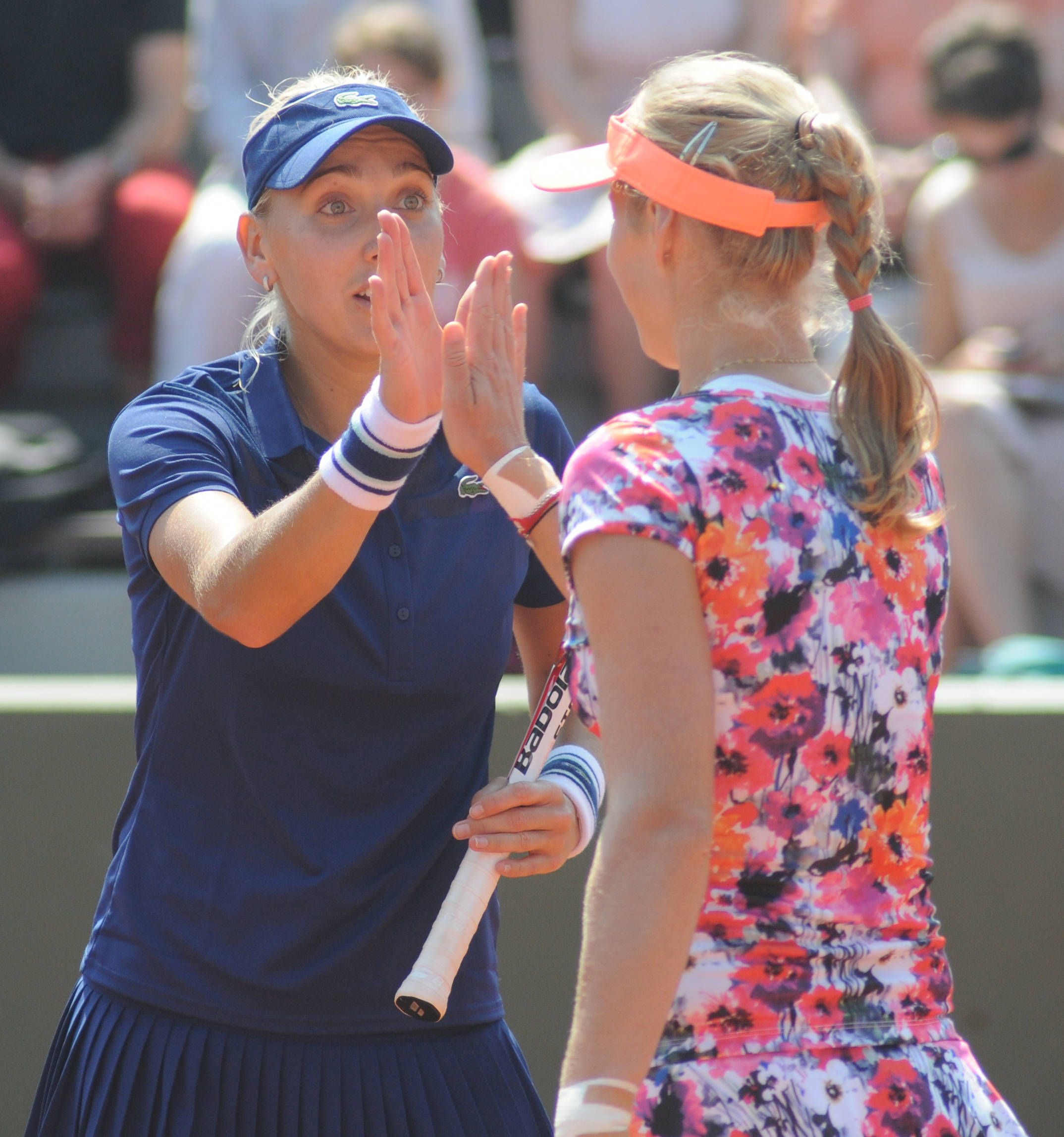 Tennis 桌布 壁紙 — 兩位女網球運動員在陽光明媚的紅土球場上擊掌，背景有觀眾。