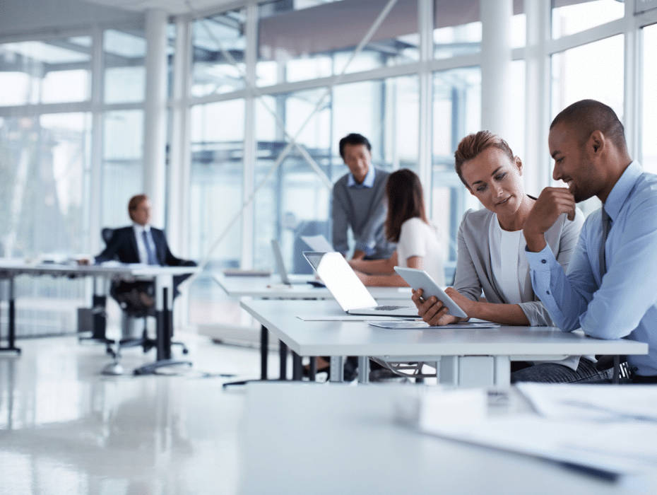 Working 桌布 壁紙 — 兩位專業人士在一個明亮現代、設有大窗戶的開放式辦公室中，專注地協作使用平板電腦。