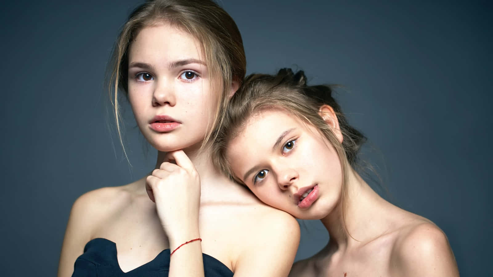 girls 桌布 壁紙 — 兩位年輕女性在柔和的灰色背景下親密擺姿勢，其中一人將頭靠在另一人的肩膀上。